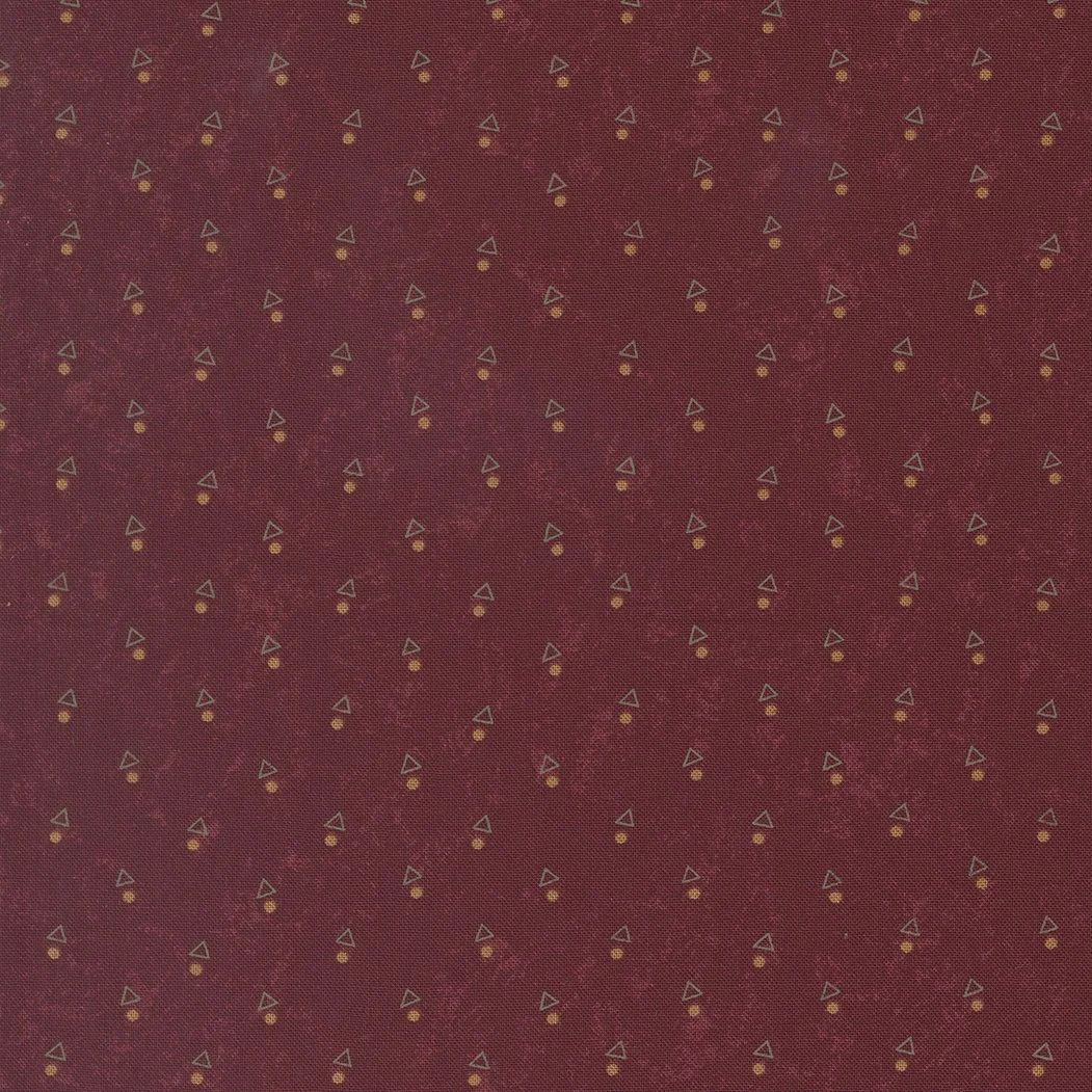 Close-up of dark red fabric with small yellow circles and gray triangle patterns evenly spaced.