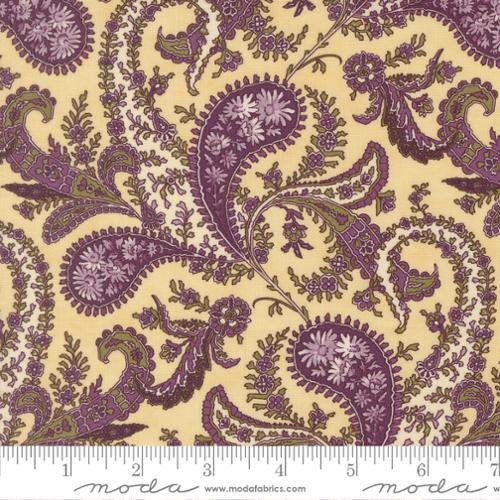 Close-up of fabric with a purple and green paisley floral pattern on a beige background, with a ruler showing inches at the bottom.