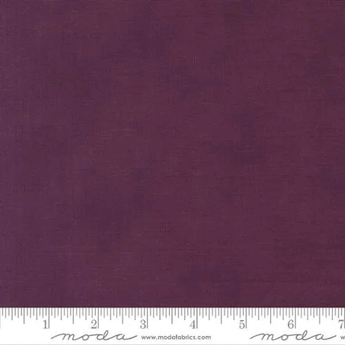 Close-up of a solid dark purple fabric with a measuring ruler at the bottom, labeled 'moda fabrics'.