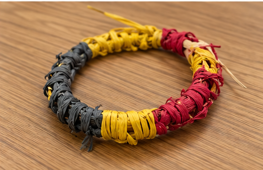 Handwoven bracelet in yellow, red and black on a wooden surface.