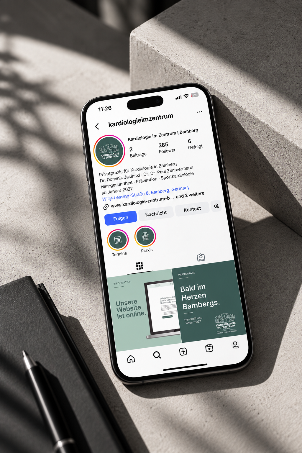 Smartphone zeigt die Instagram-Seite von einer Kardiologie-Praxis in Bamberg, Deutschland, mit Informationen zur Praxis und Online-Website, das auf einem Tisch liegt.