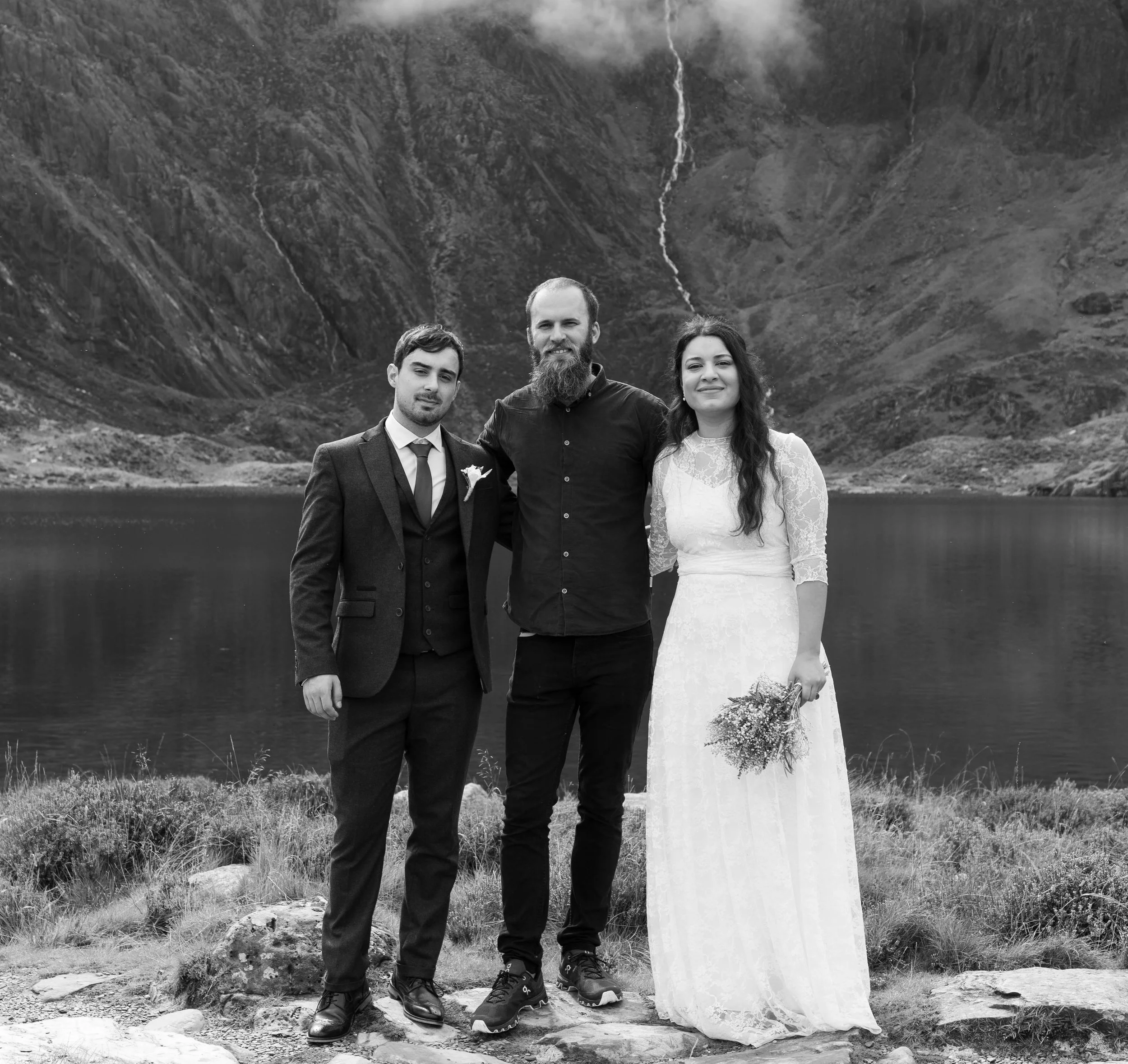Black and white photo of a couple standing with Leon beside a mountain lake