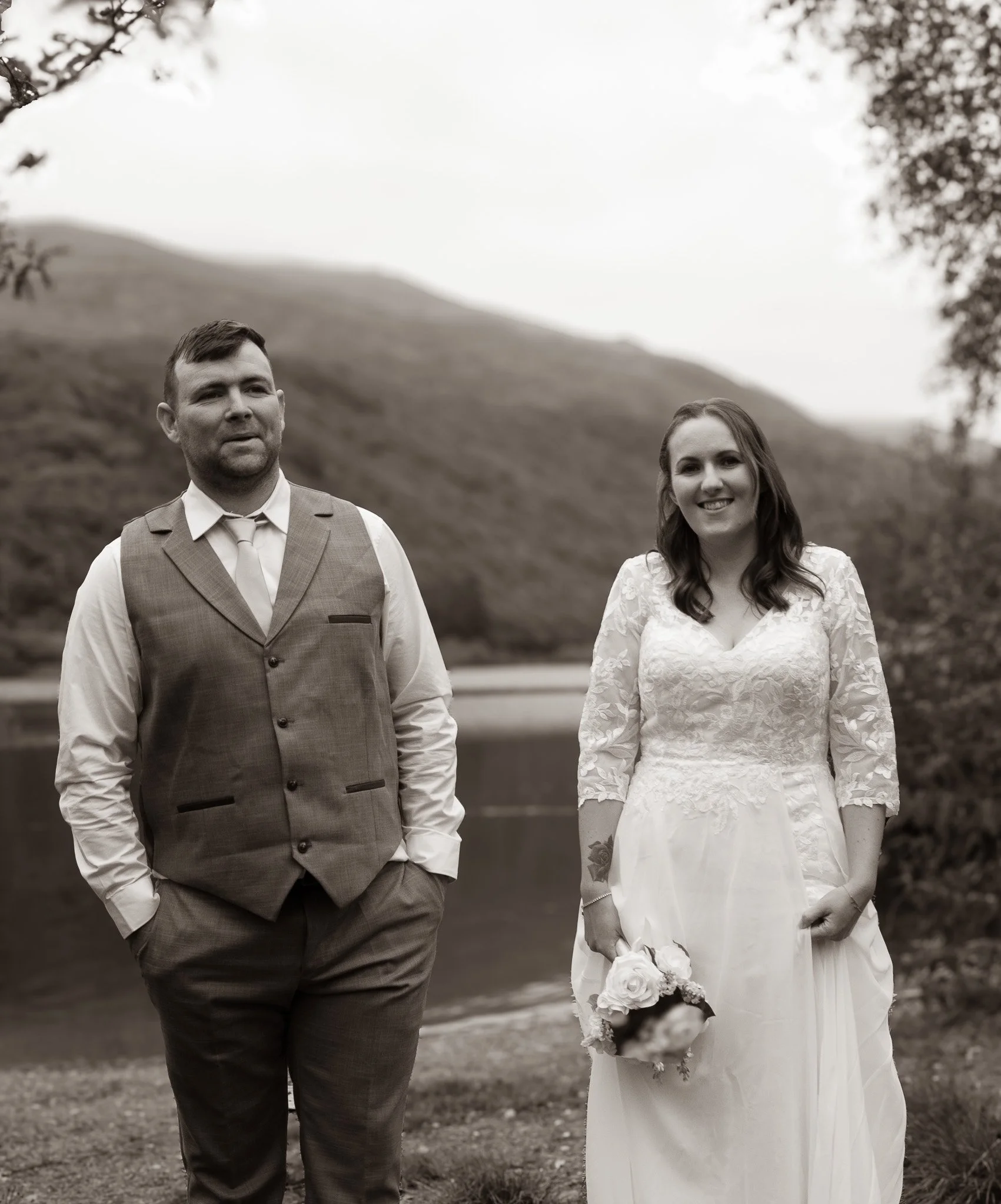 Couple standing side by side in front of a lake, in black and white