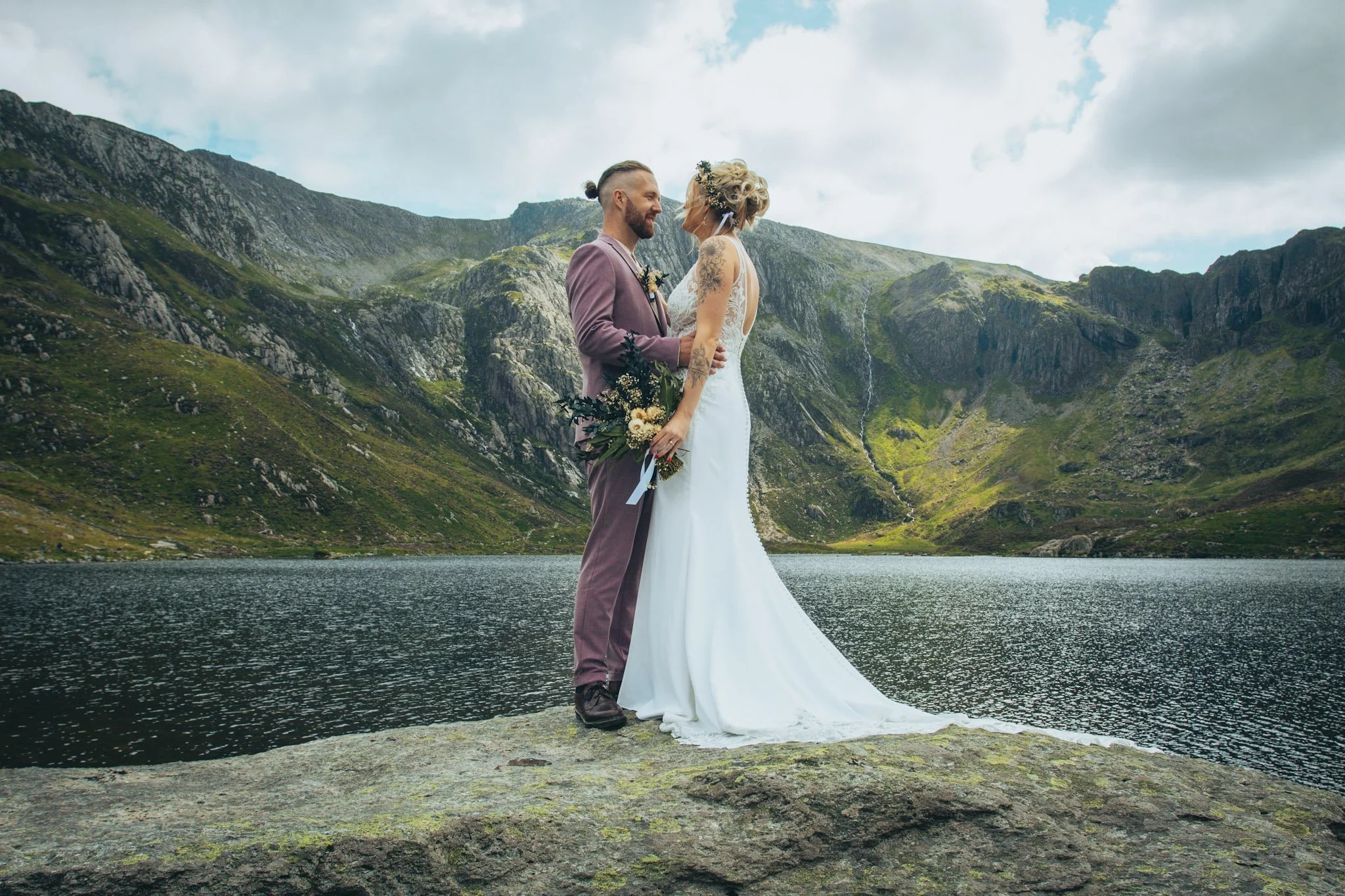 A couple kissing on a rock beside a mountain lake