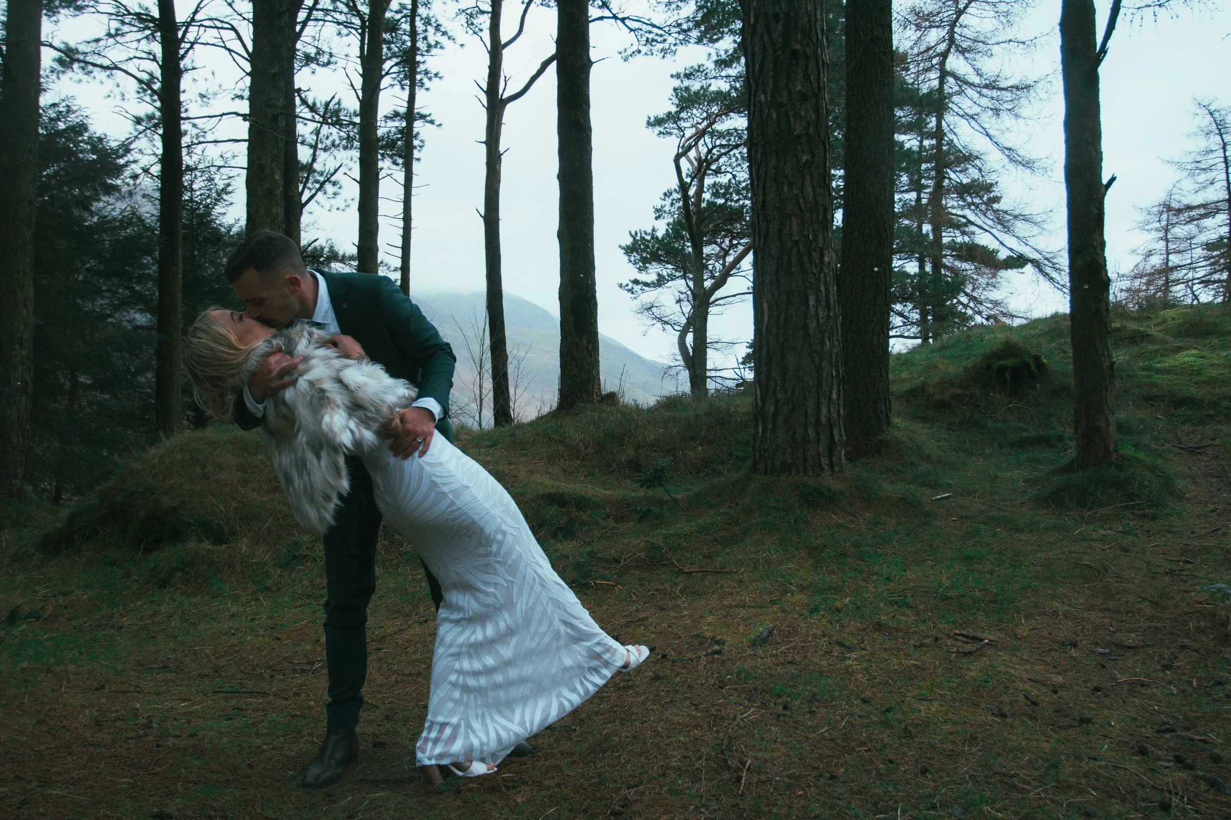 A groom dipping his bride for a kiss in a pine forest