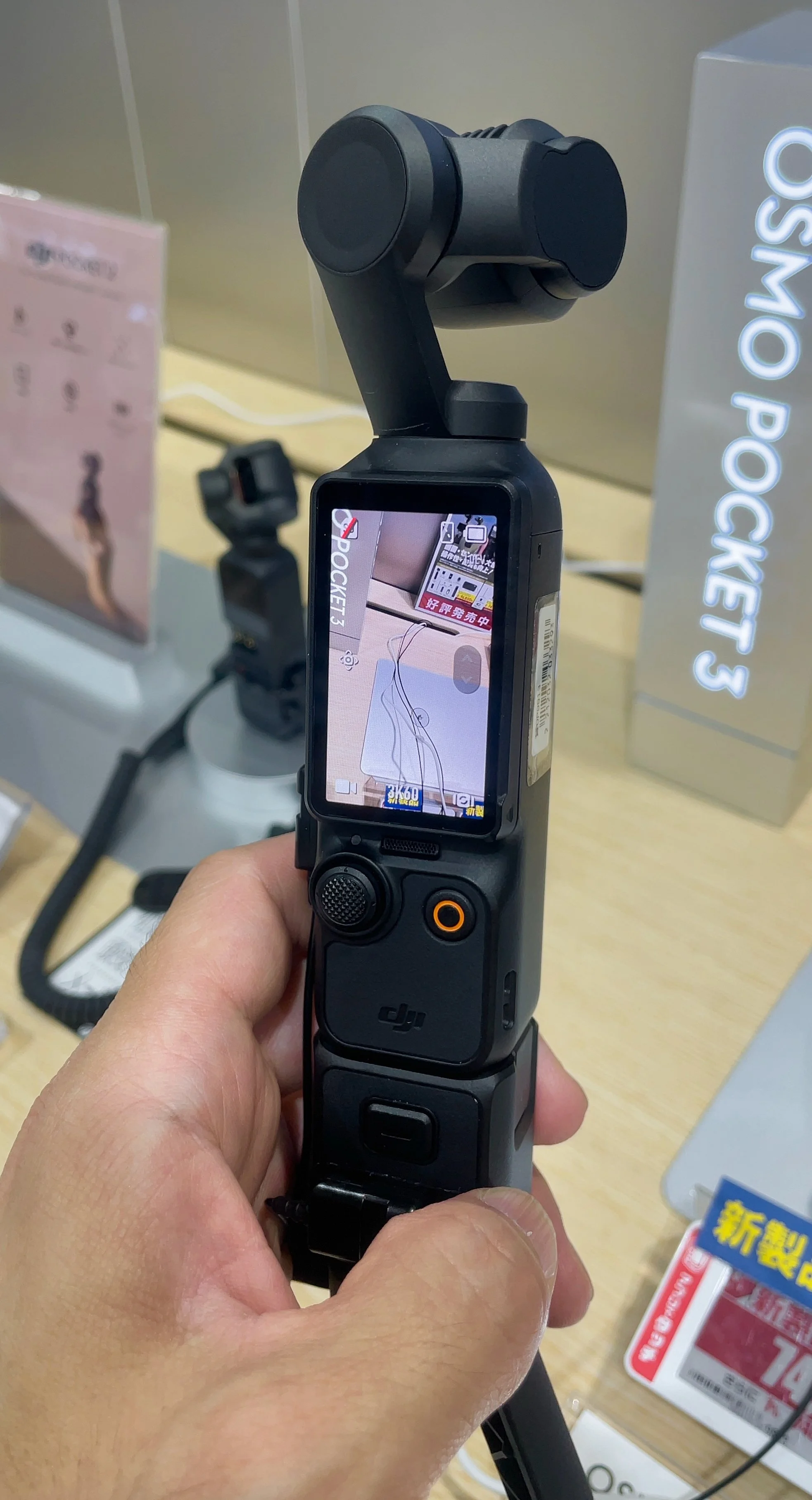 A hand holding a DJI Osmo Pocket 3 video camera on a shop display (stock photograph of that model)