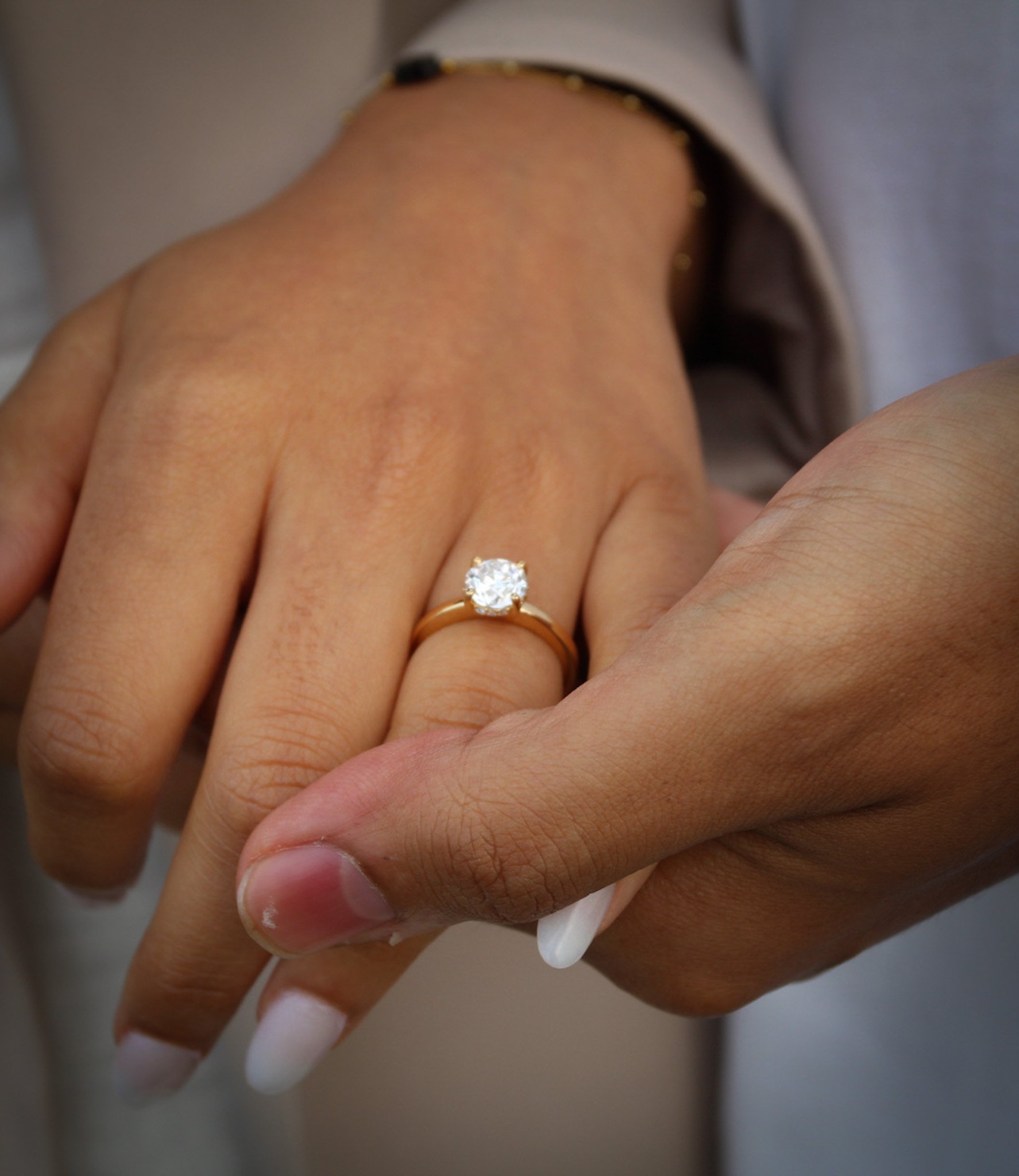 Close-up of a hand with a diamond engagement ring resting in a partner's hand