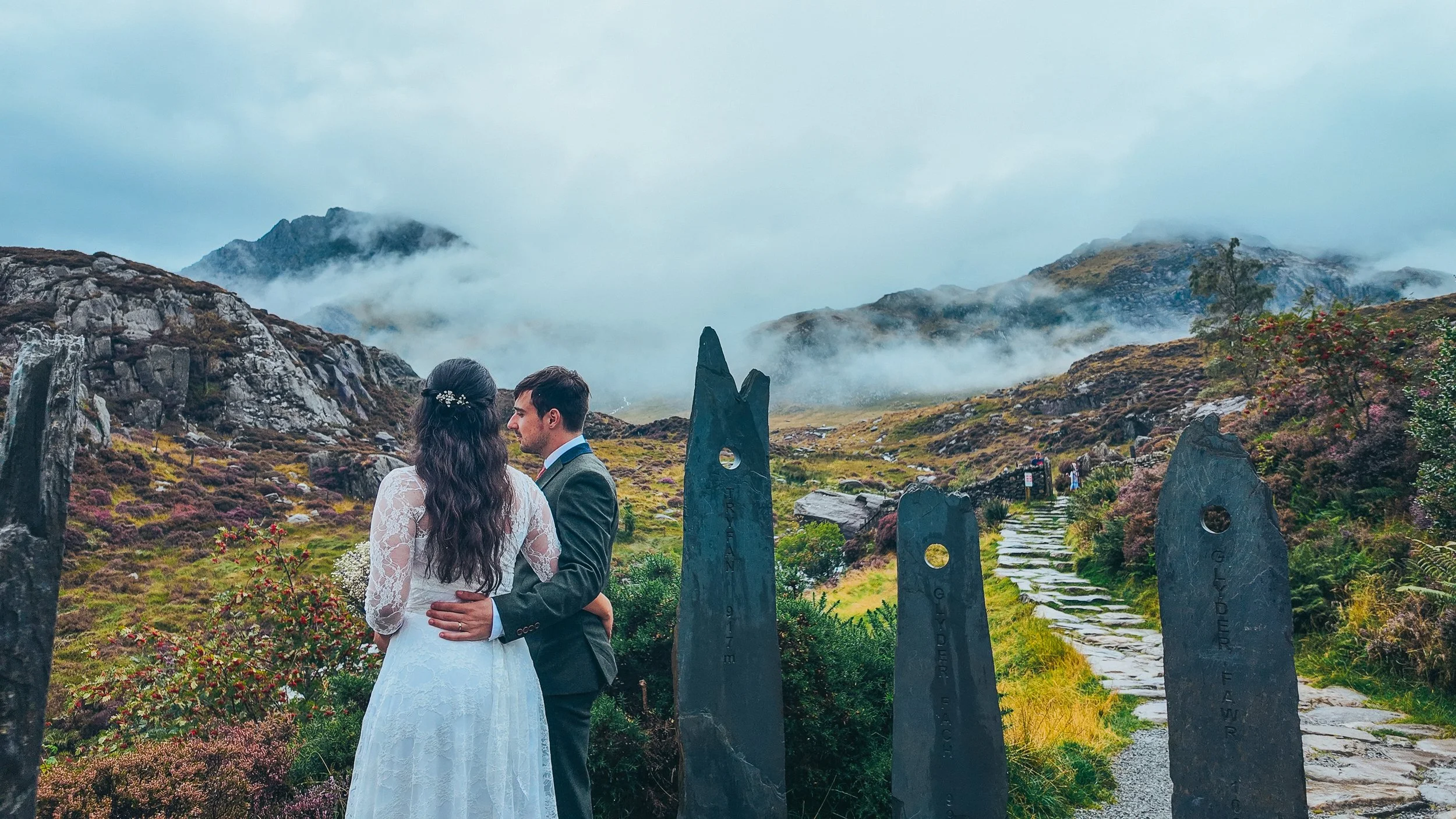 Couple embracing on a stone path between standing stones, mist over the mountains