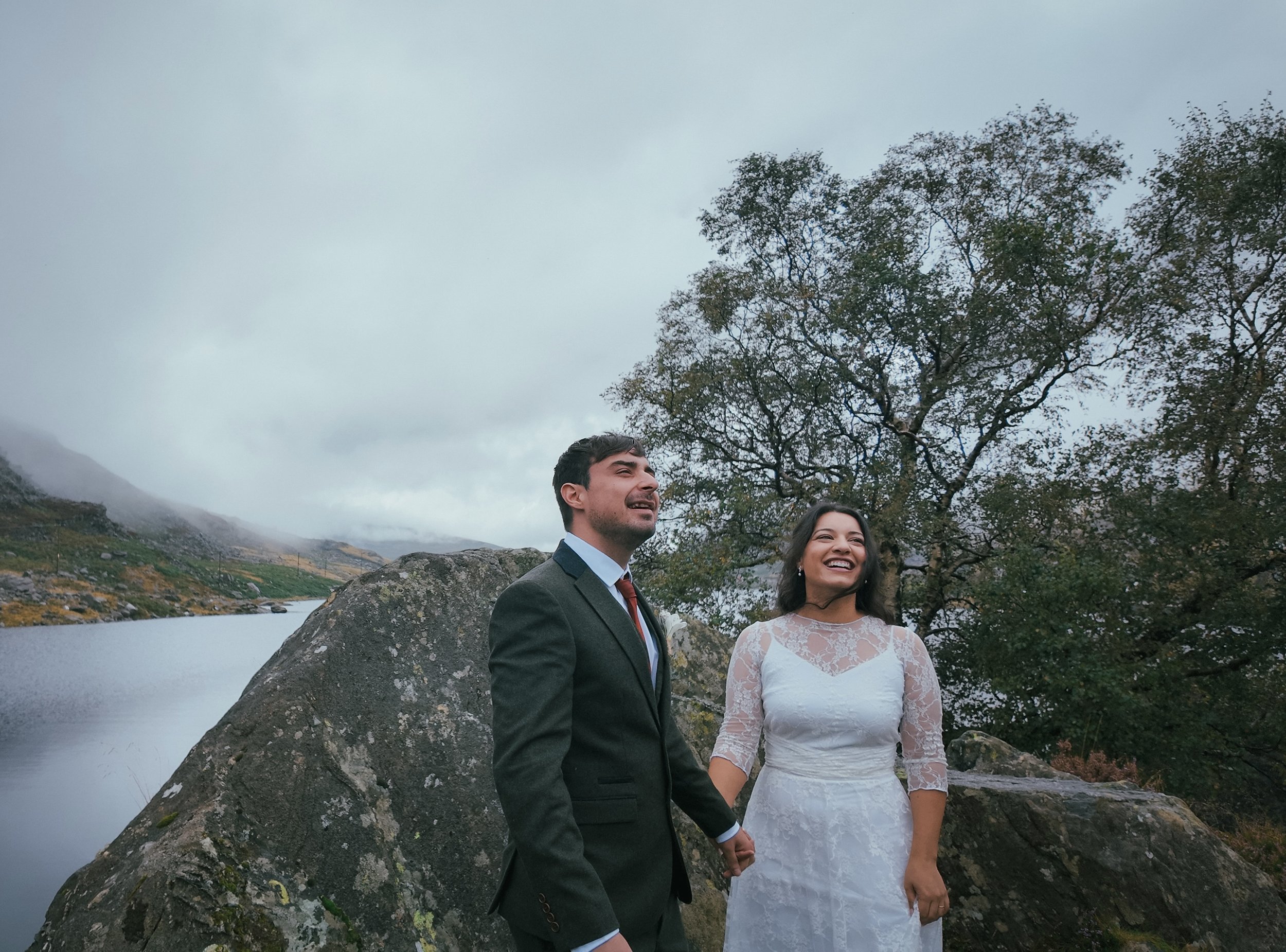 A couple holding hands beside a large boulder by a lake