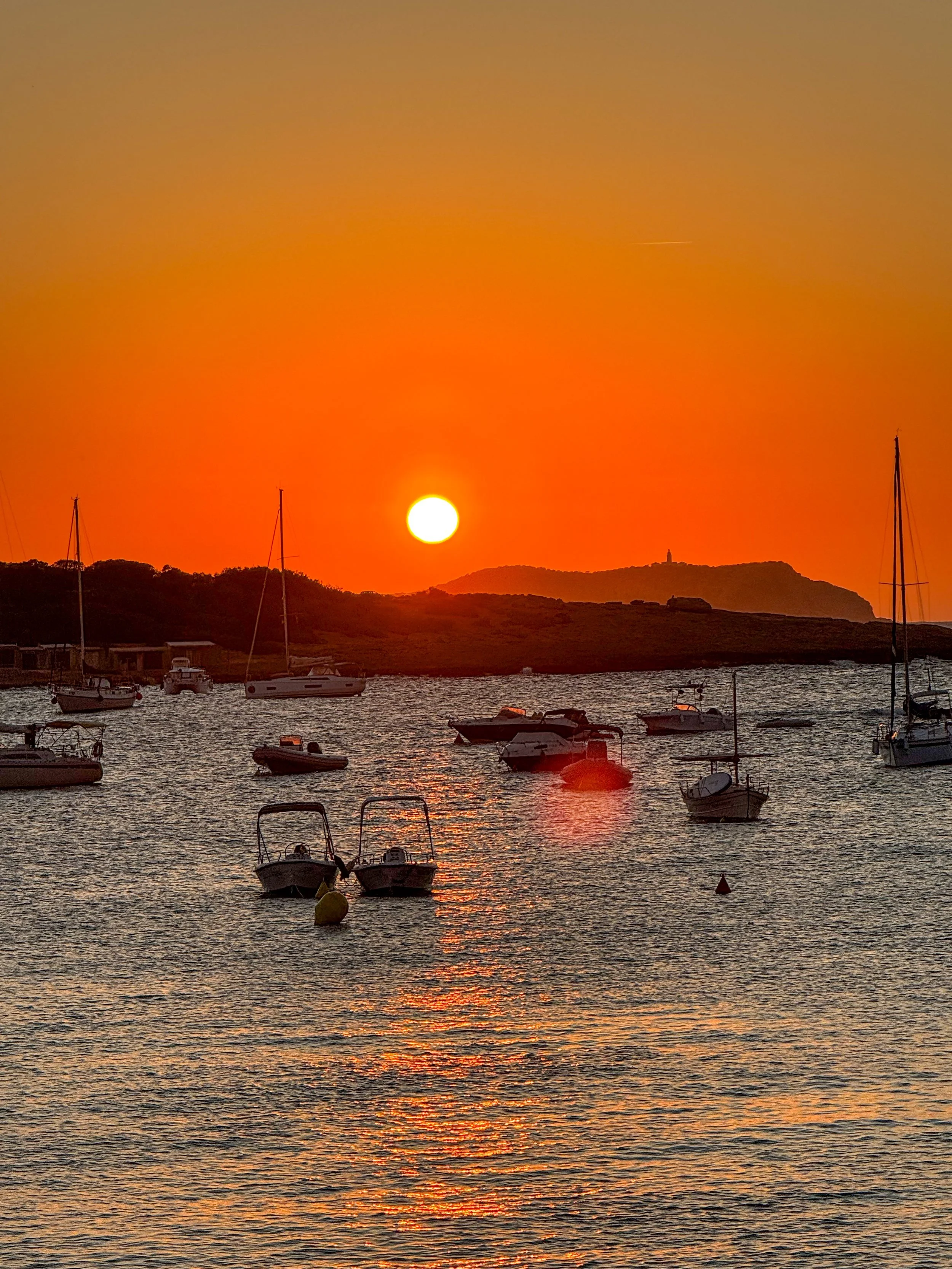 An orange sun setting over a harbour with small boats moored on the water