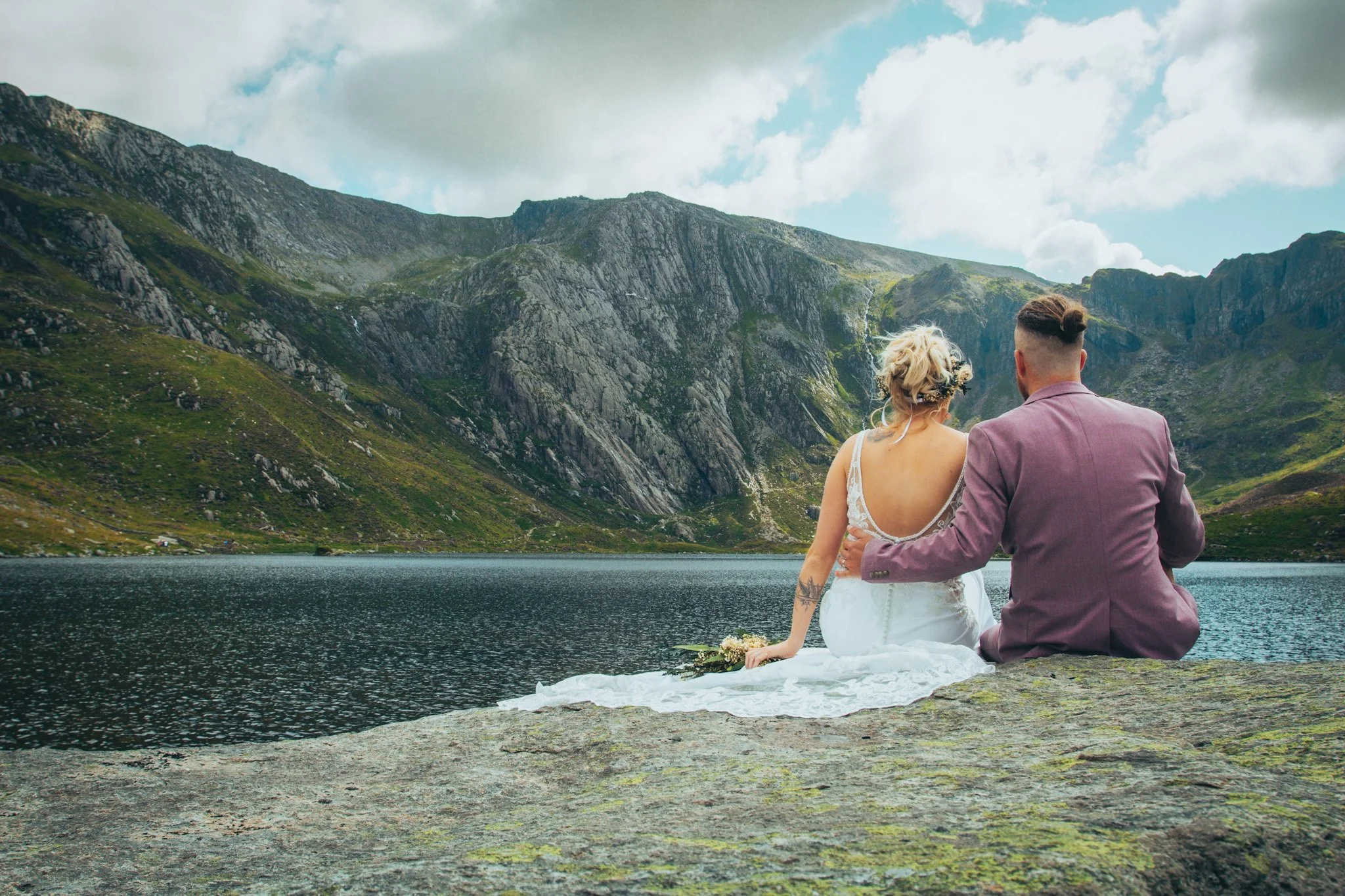 A couple sitting together on a rock beside a mountain lake