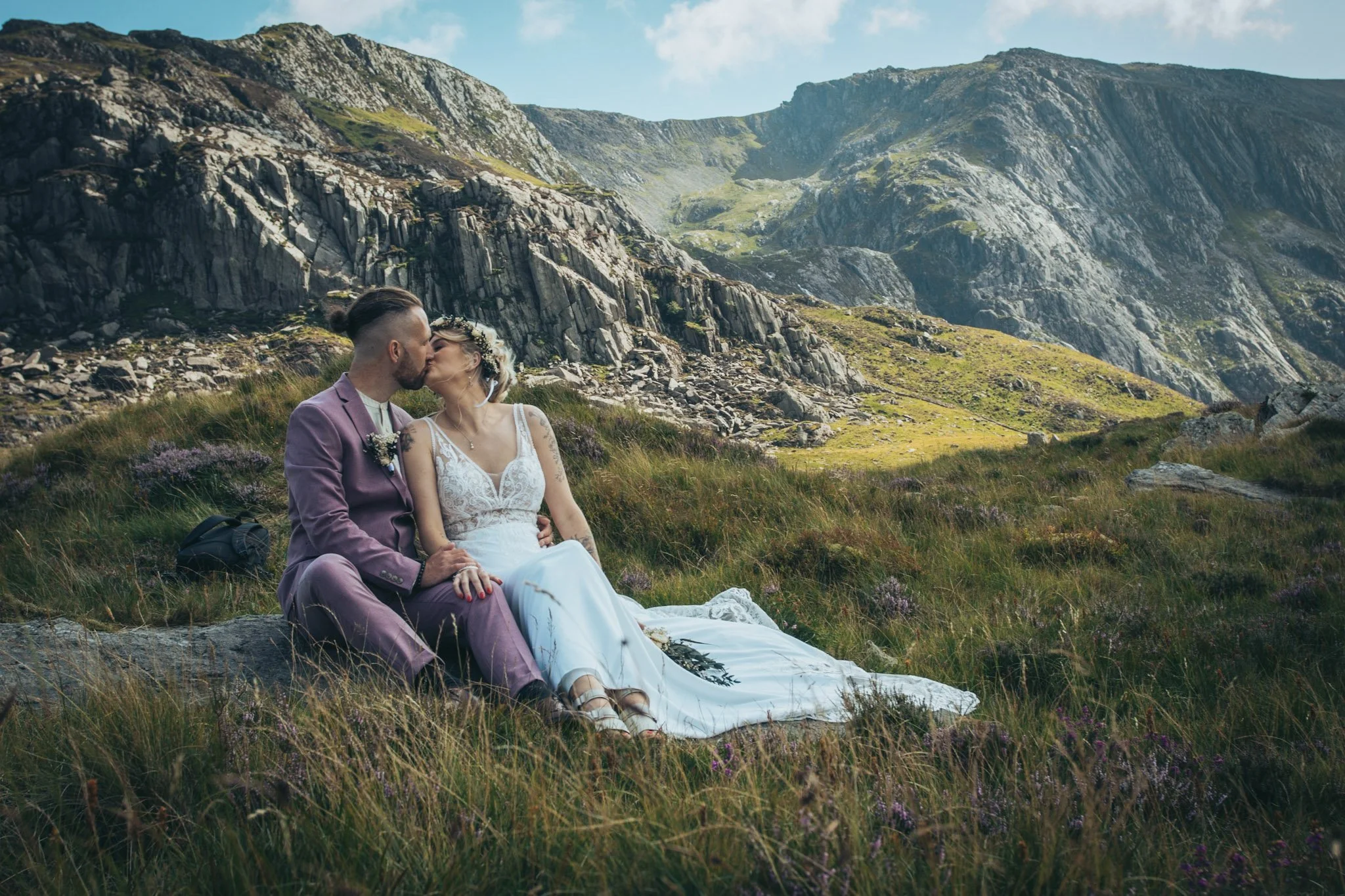 A couple kissing while sitting on the grass in a mountain valley