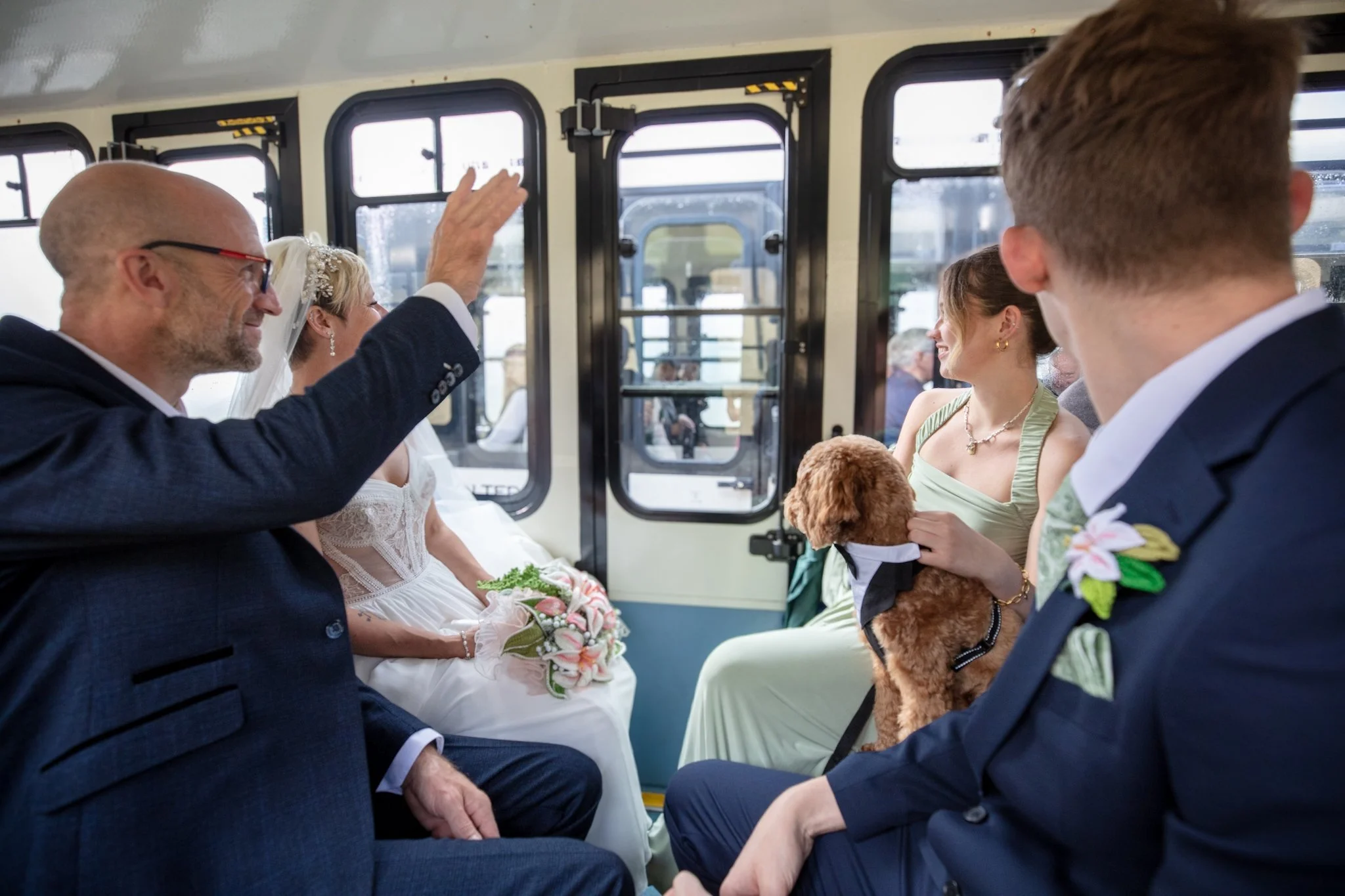 Wedding guests seated inside a carriage, one raising a hand