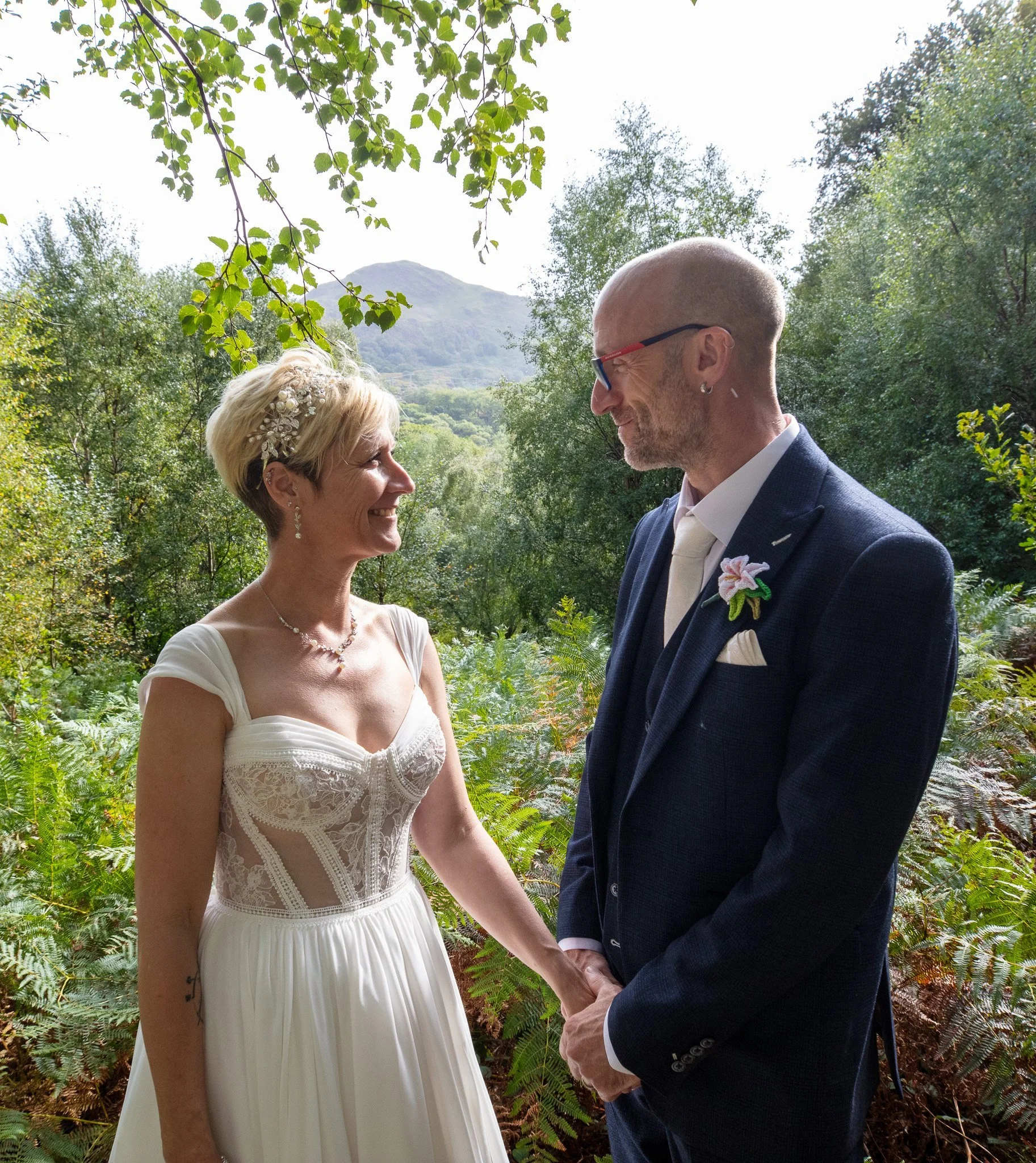 A bride and groom holding hands among ferns and trees
