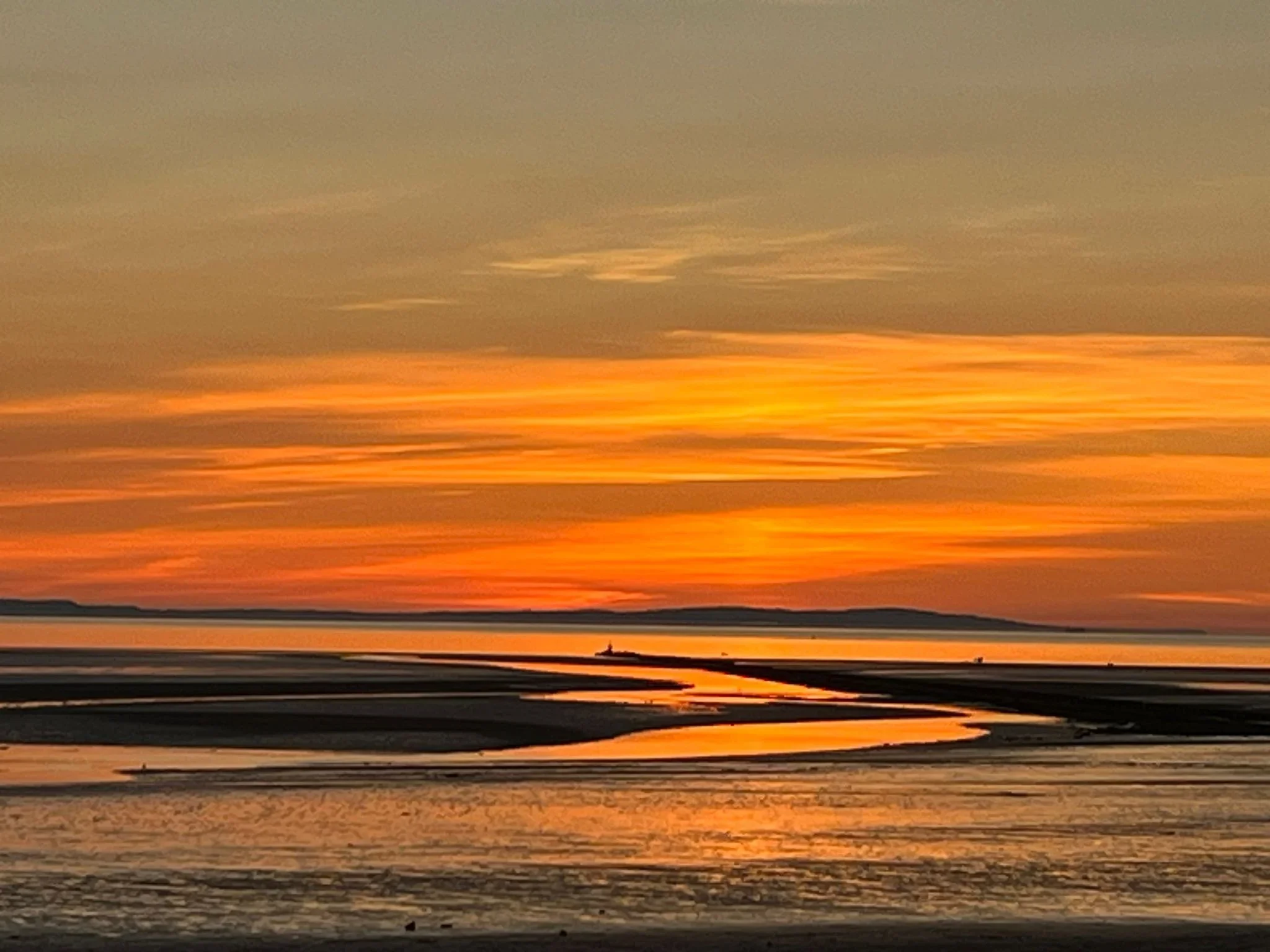 An orange and gold sunset reflected across a beach at low tide