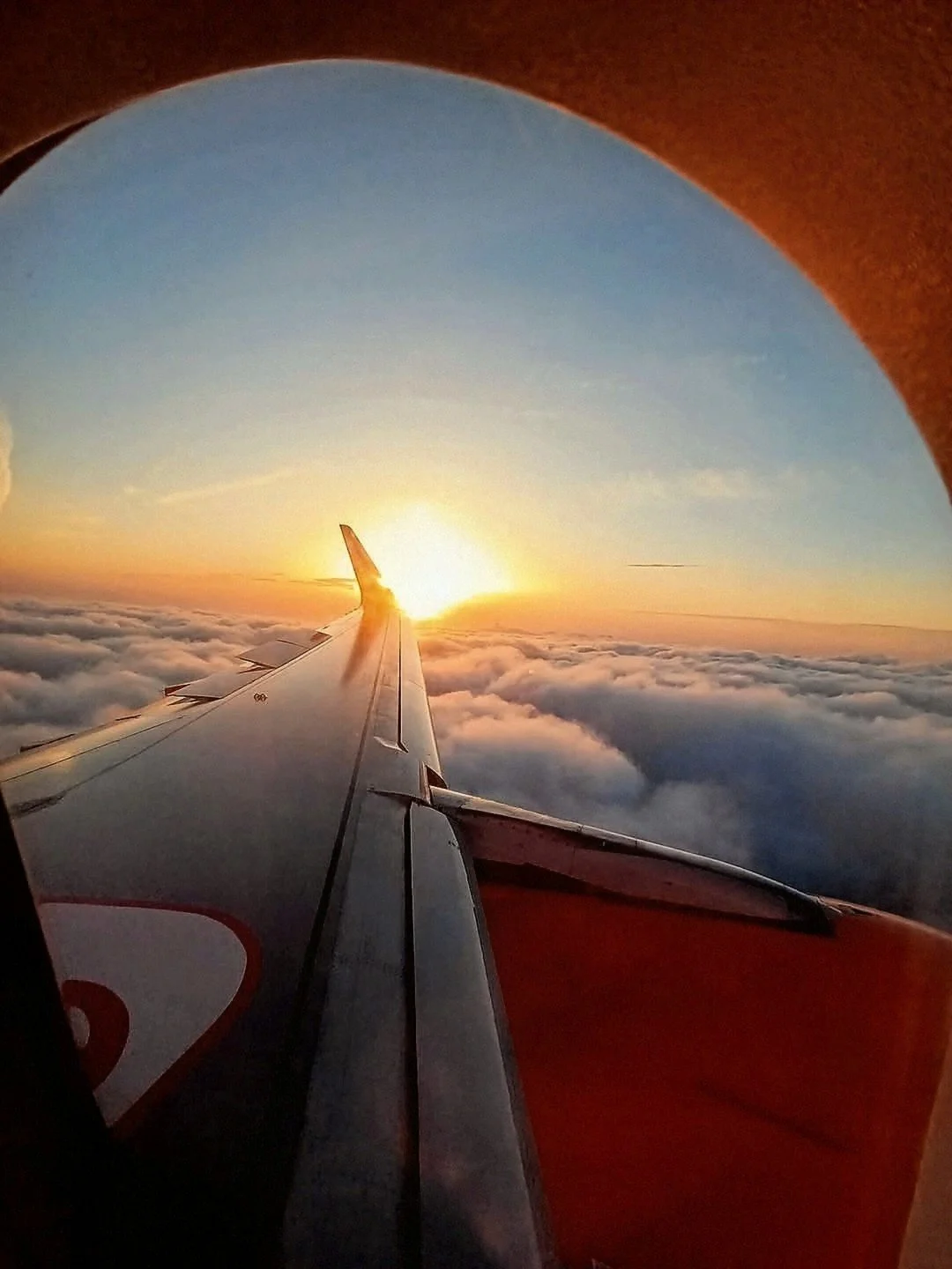 A view from an aeroplane window of the wing and the sun setting above a layer of cloud