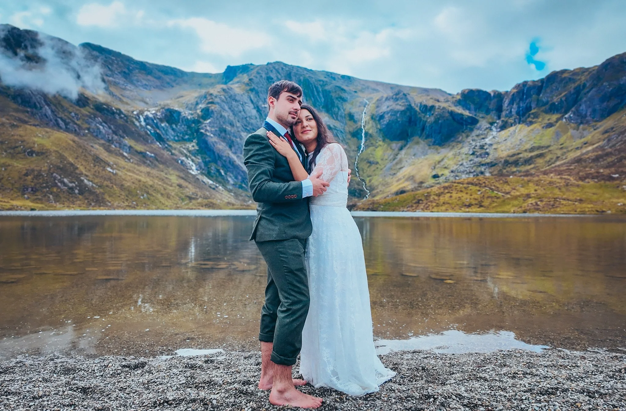 Couple embracing barefoot on the shore of a mountain lake