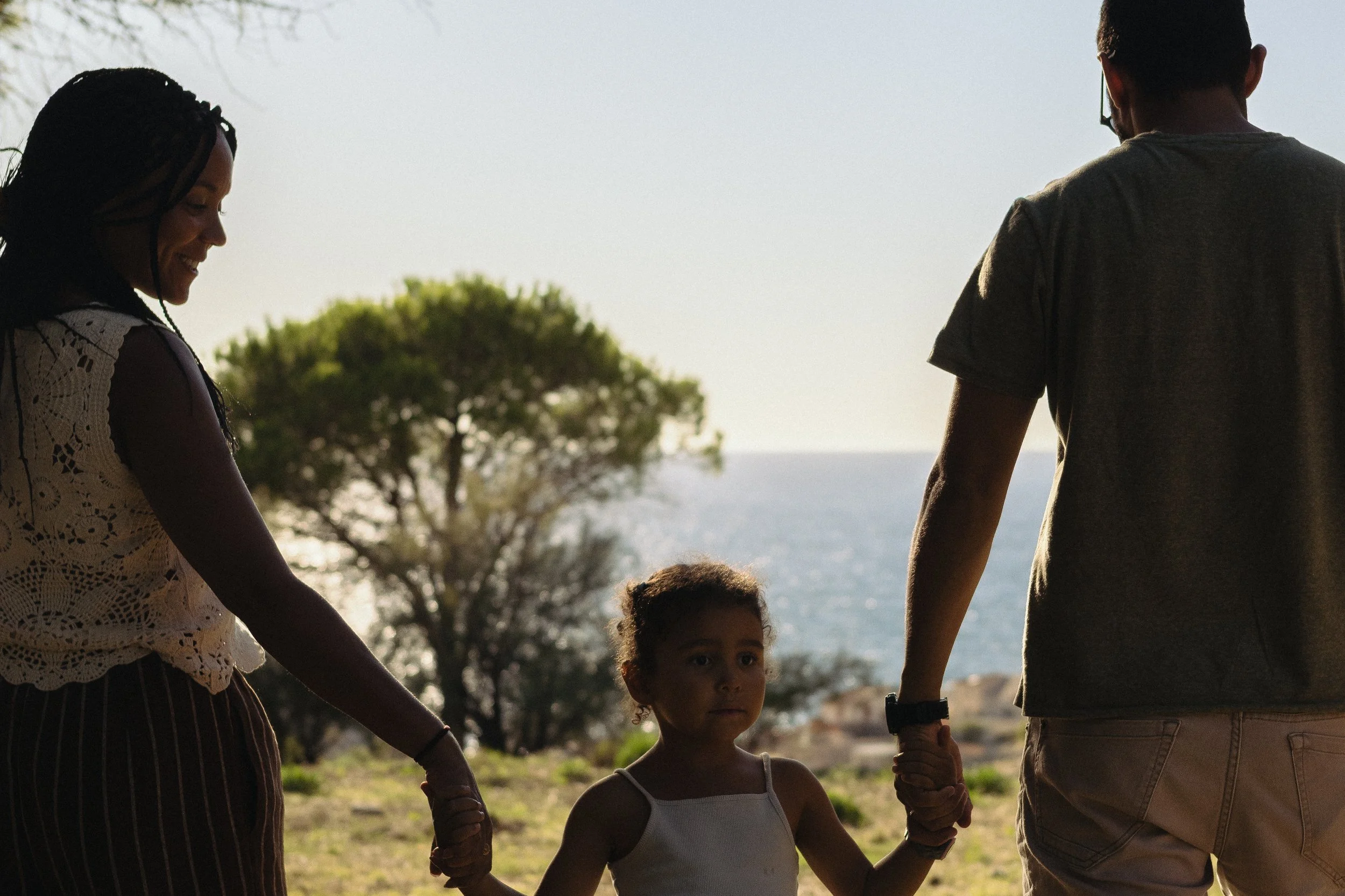 Photo de trois enfants et deux adultes qui tiennent des mains, arrière-plan de nature avec un arbre et la mer