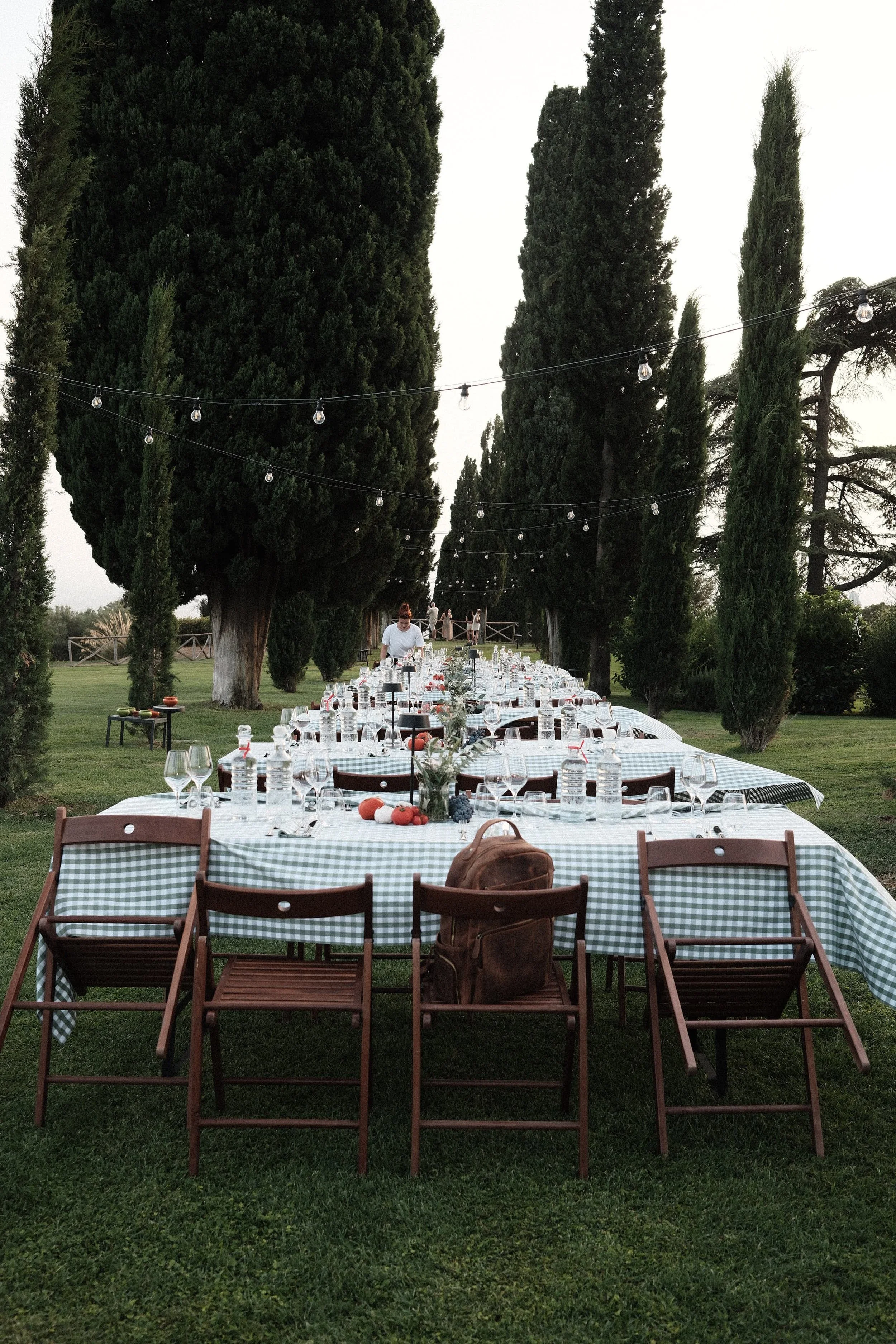 Sfeervol gedekte dinertafel in een tuin in Toscane, omringd door cipressen en lichtslingers.