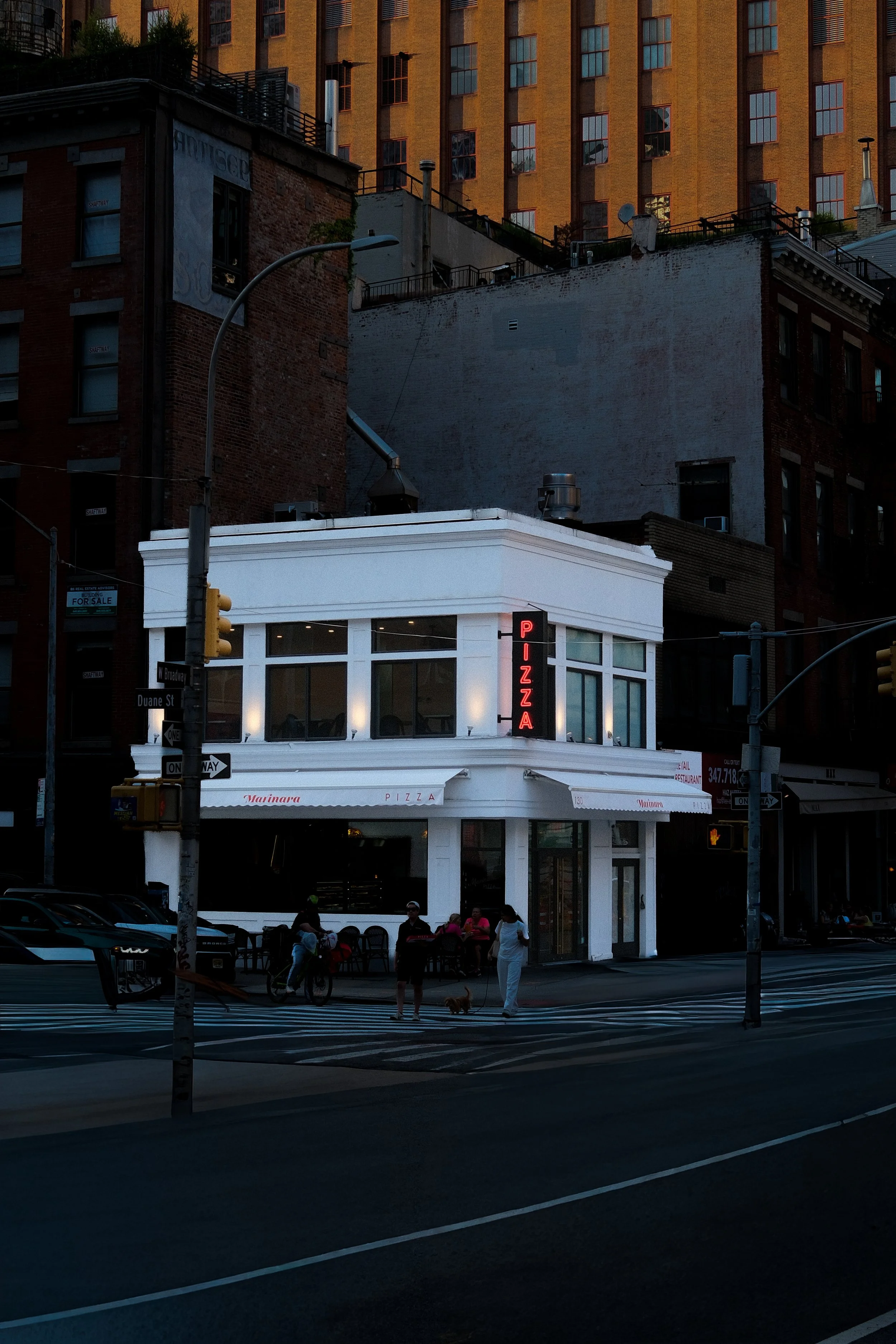 Avondfoto van een levendige straat met pizzeria en voorbijgangers in New York.