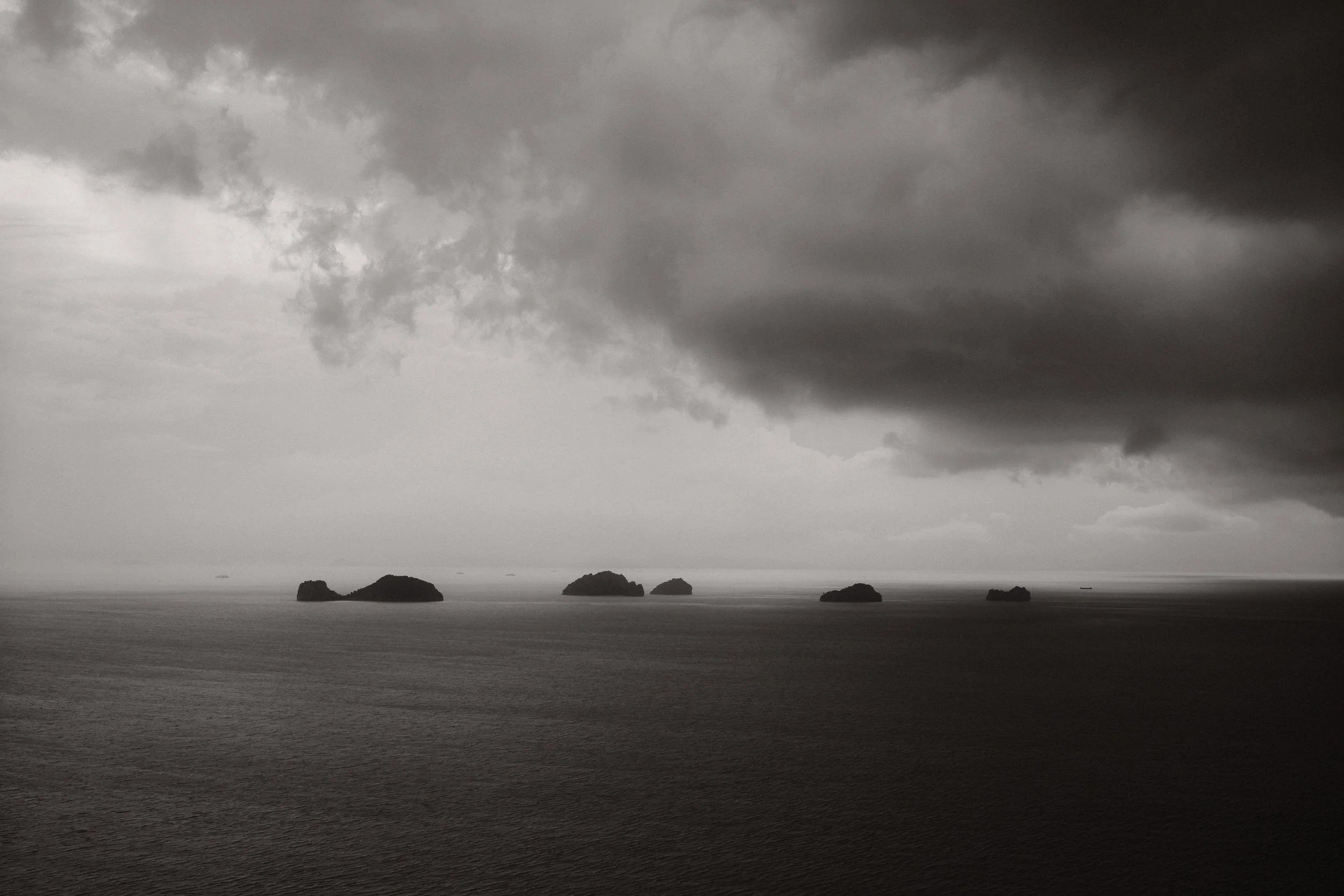 Zwart-wit landschapsfoto van een bewolkte zee met kleine eilanden voor de kust van Thailand.