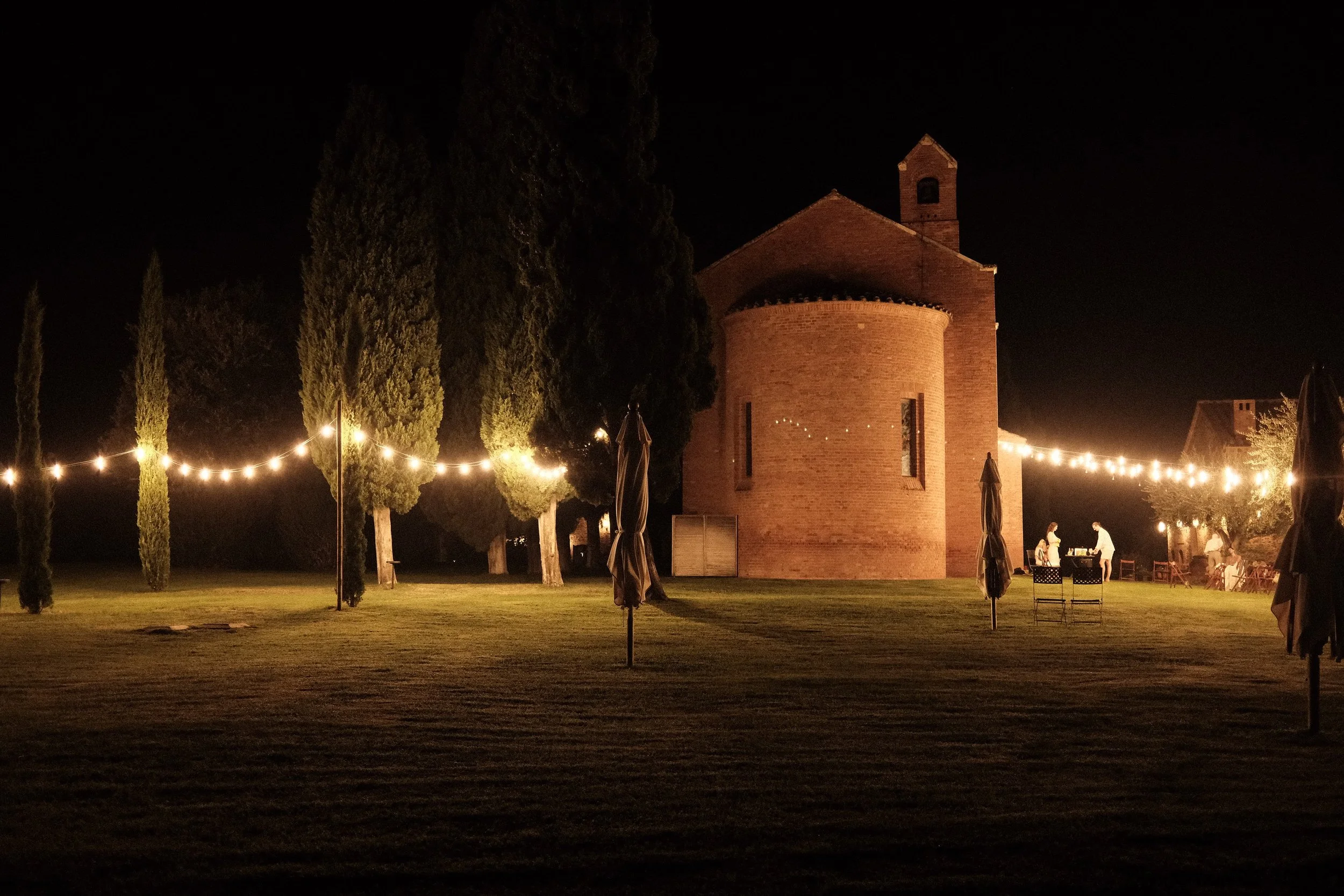 Avondfeest met diner onder lichtslingers naast een historische kapel in Toscane.