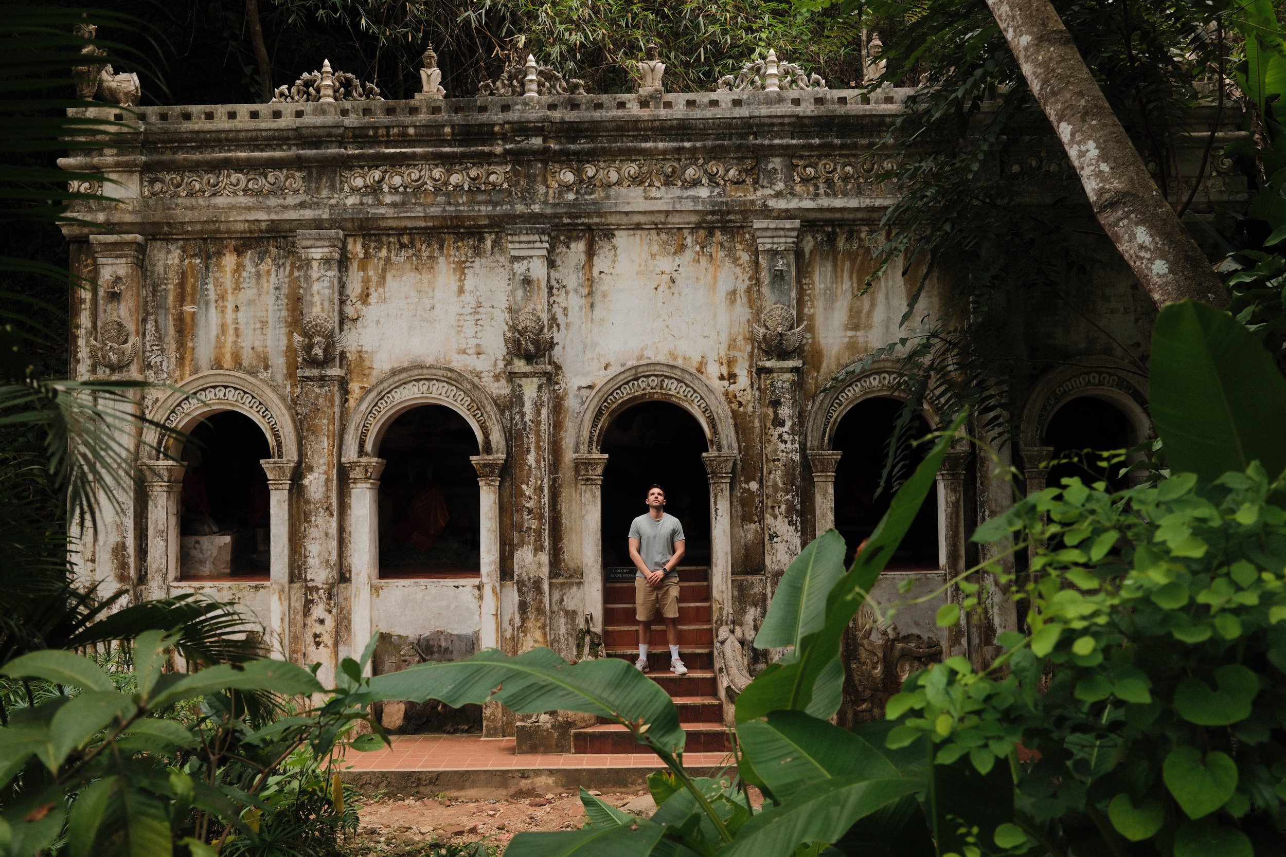 Reisportret bij een verweerd koloniaal gebouw, omringd door tropisch groen in Thailand.