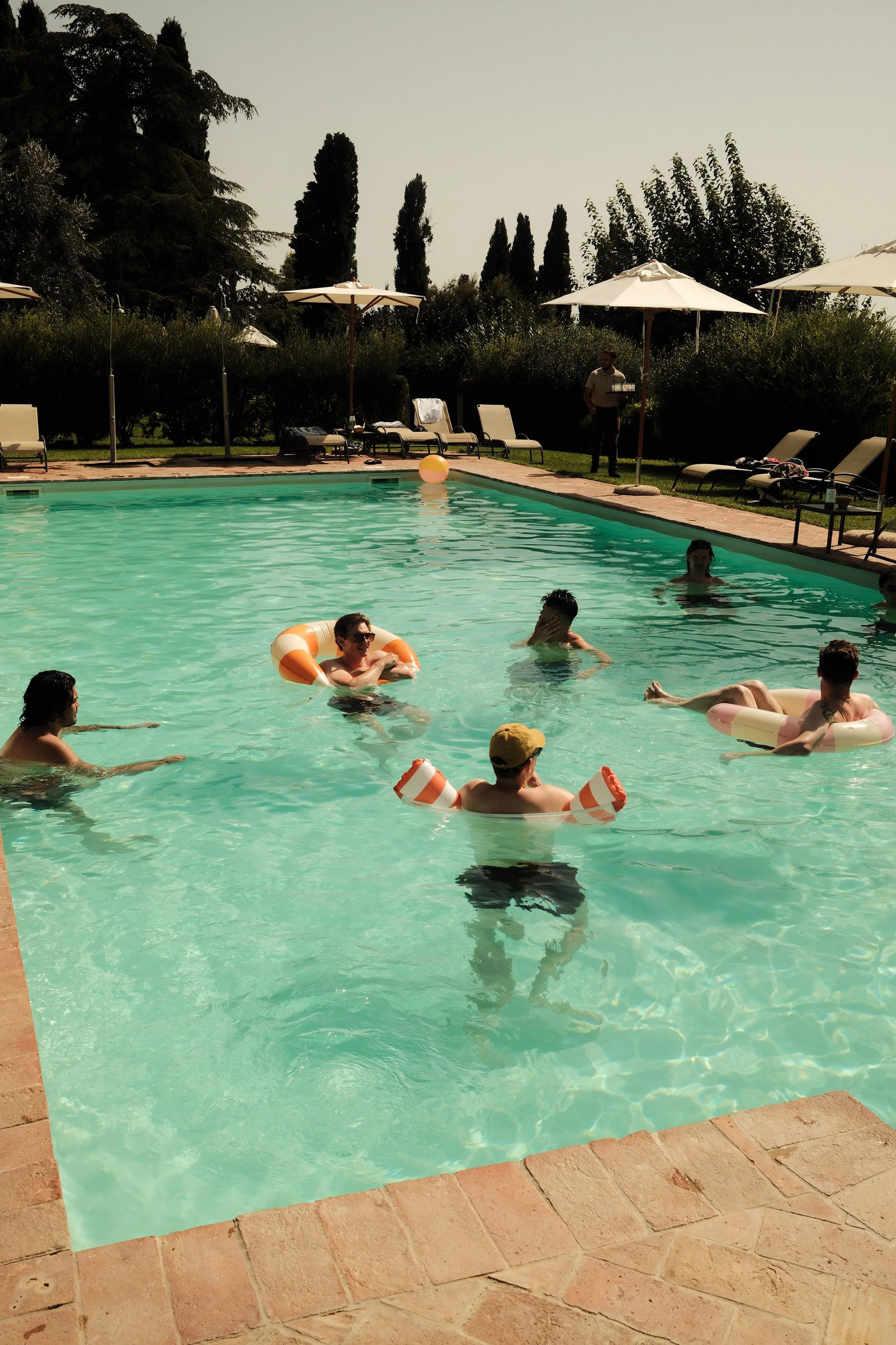 Bruiloftsgasten ontspannen bij het zwembad tijdens een zonnig trouwweekend in Toscane.
