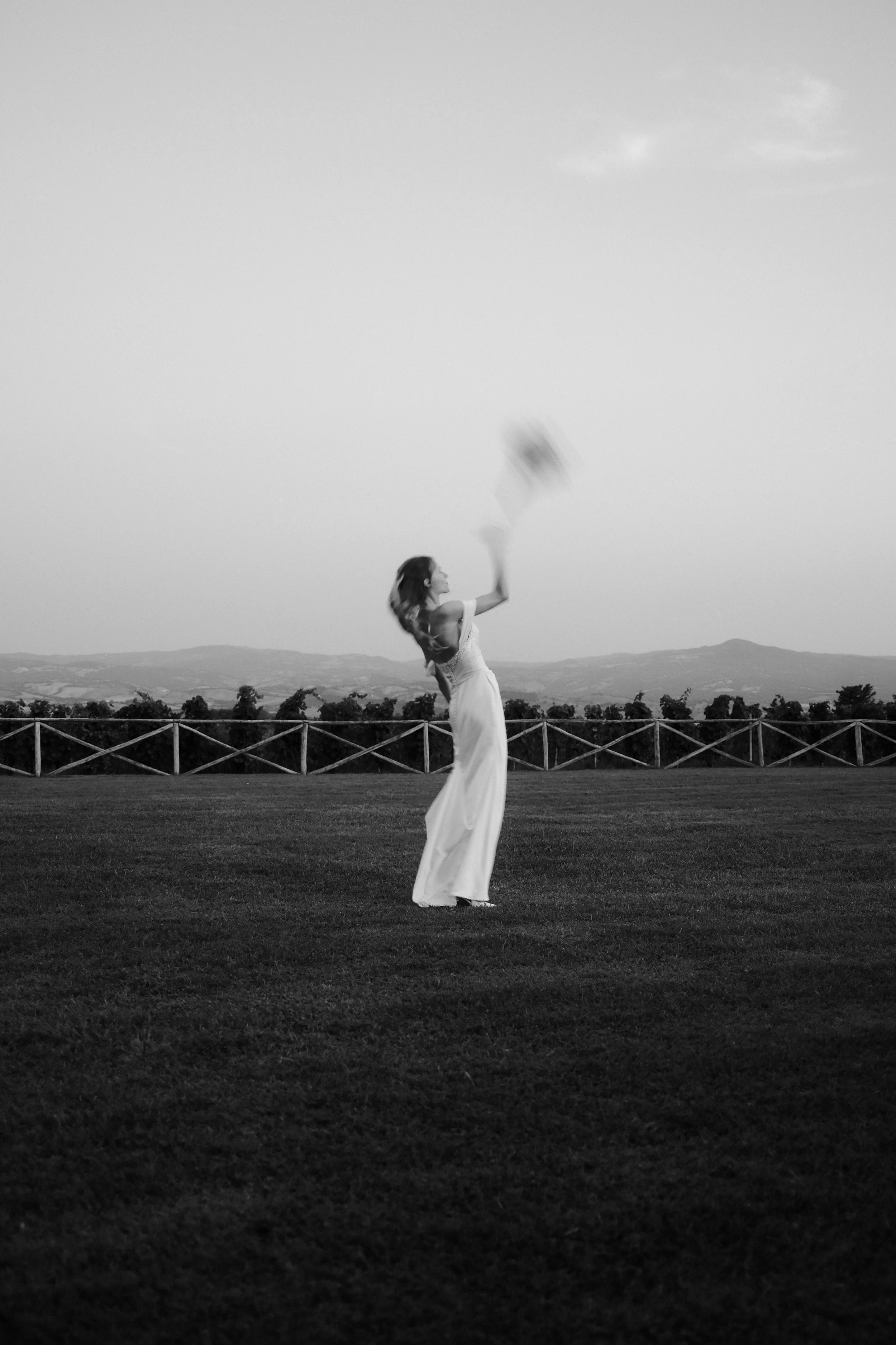 Zwart-wit portret van een vrouw in een lange jurk op een open veld in Toscane, Italië.