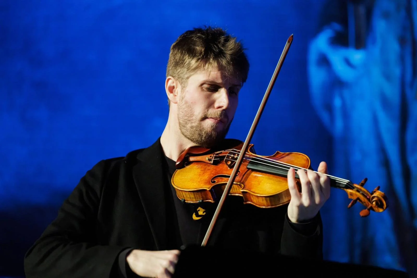 Jeune homme jouant du violon sur scène avec un fond bleu.