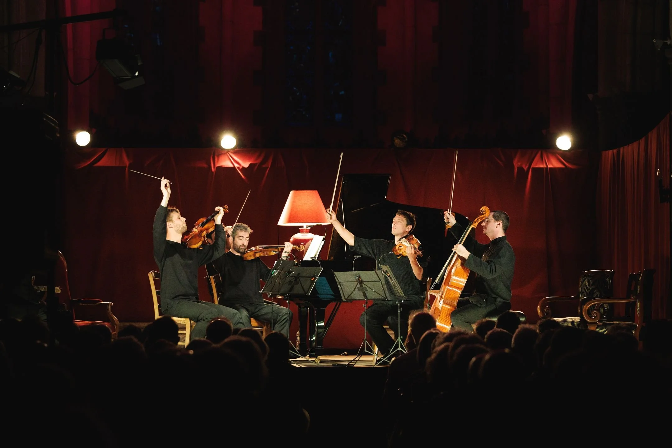 Un groupe de musiciens jouant des instruments classiques sur scène dans une salle de concert avec un rideau rouge en arrière-plan.