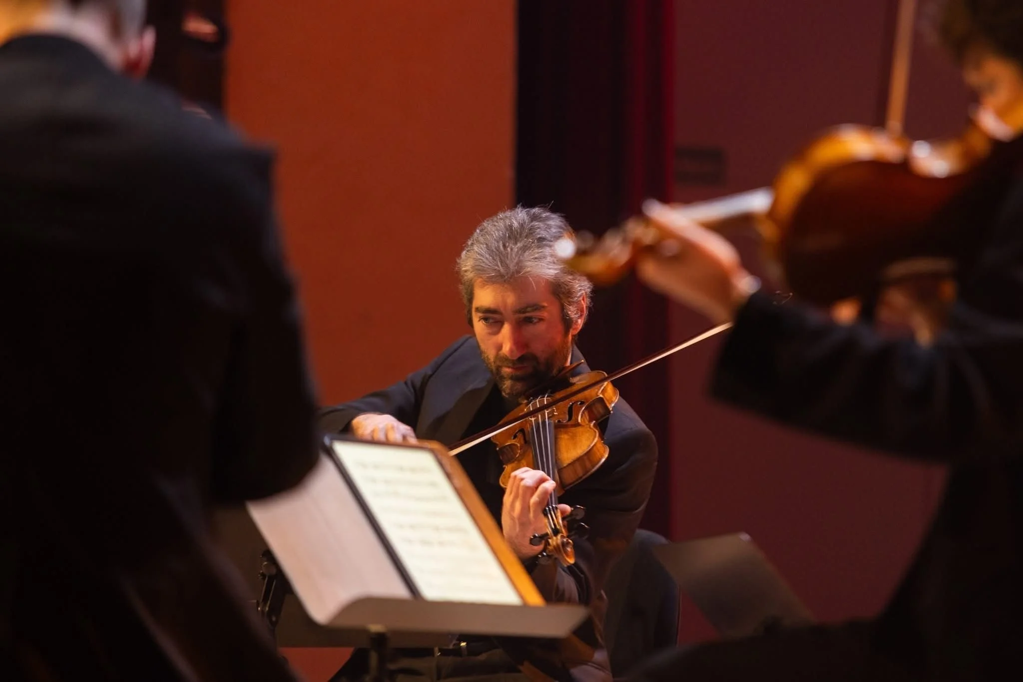 Un homme joue du violon lors d'un concert avec deux autres musiciens.