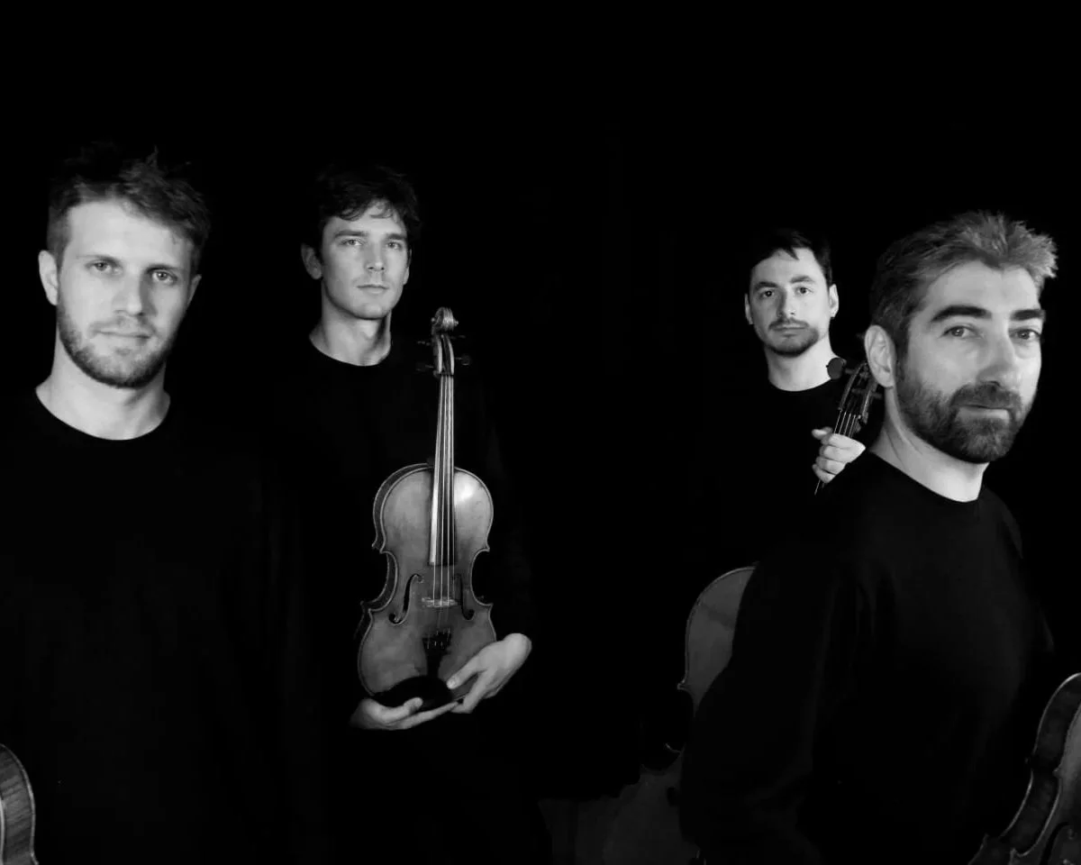 Quatre hommes posant avec leurs instruments de musique dans un fond noir, en noir et blanc.