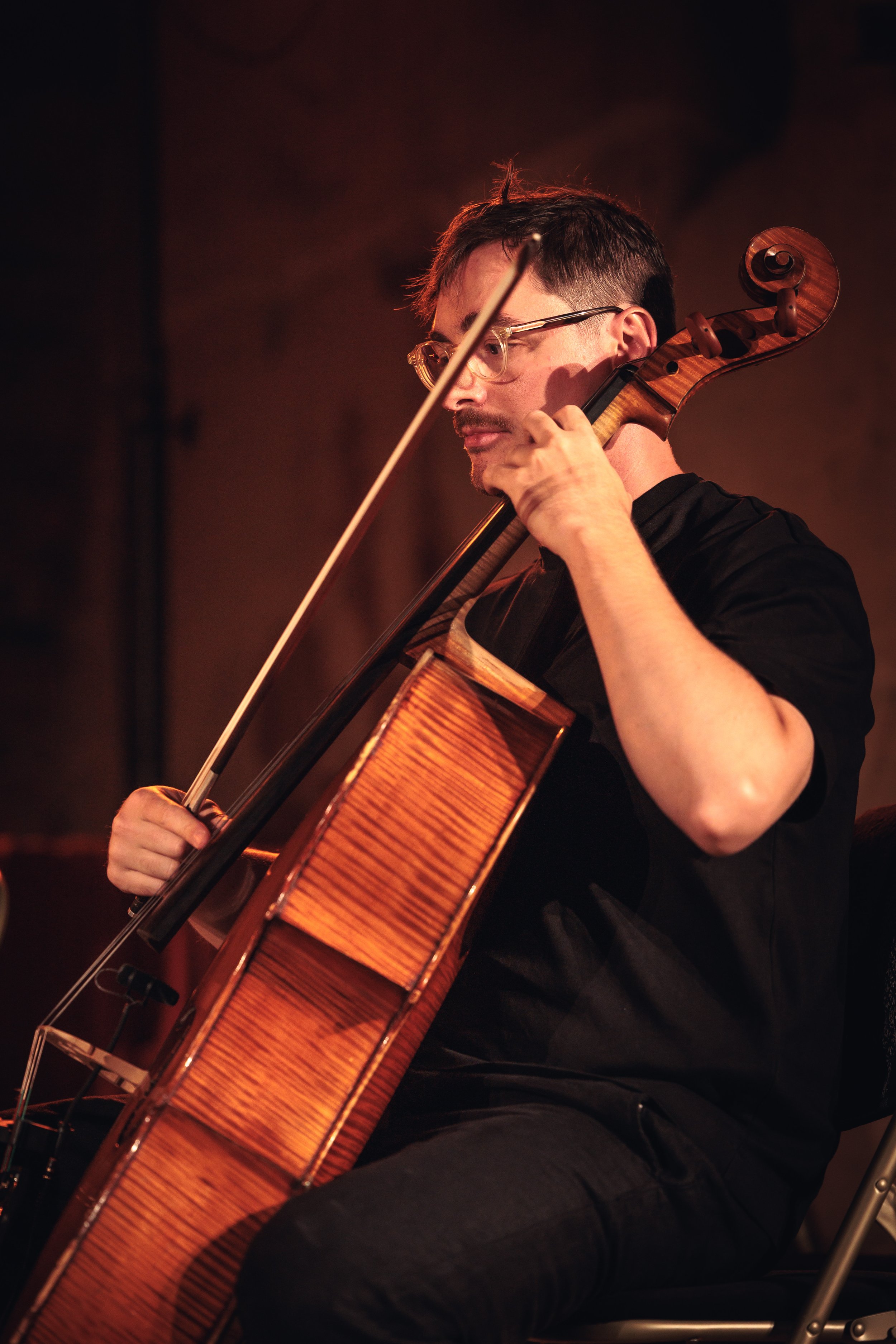 Jeune homme jouant du violon dans une pièce sombre, concentré sur son instrument en bois.