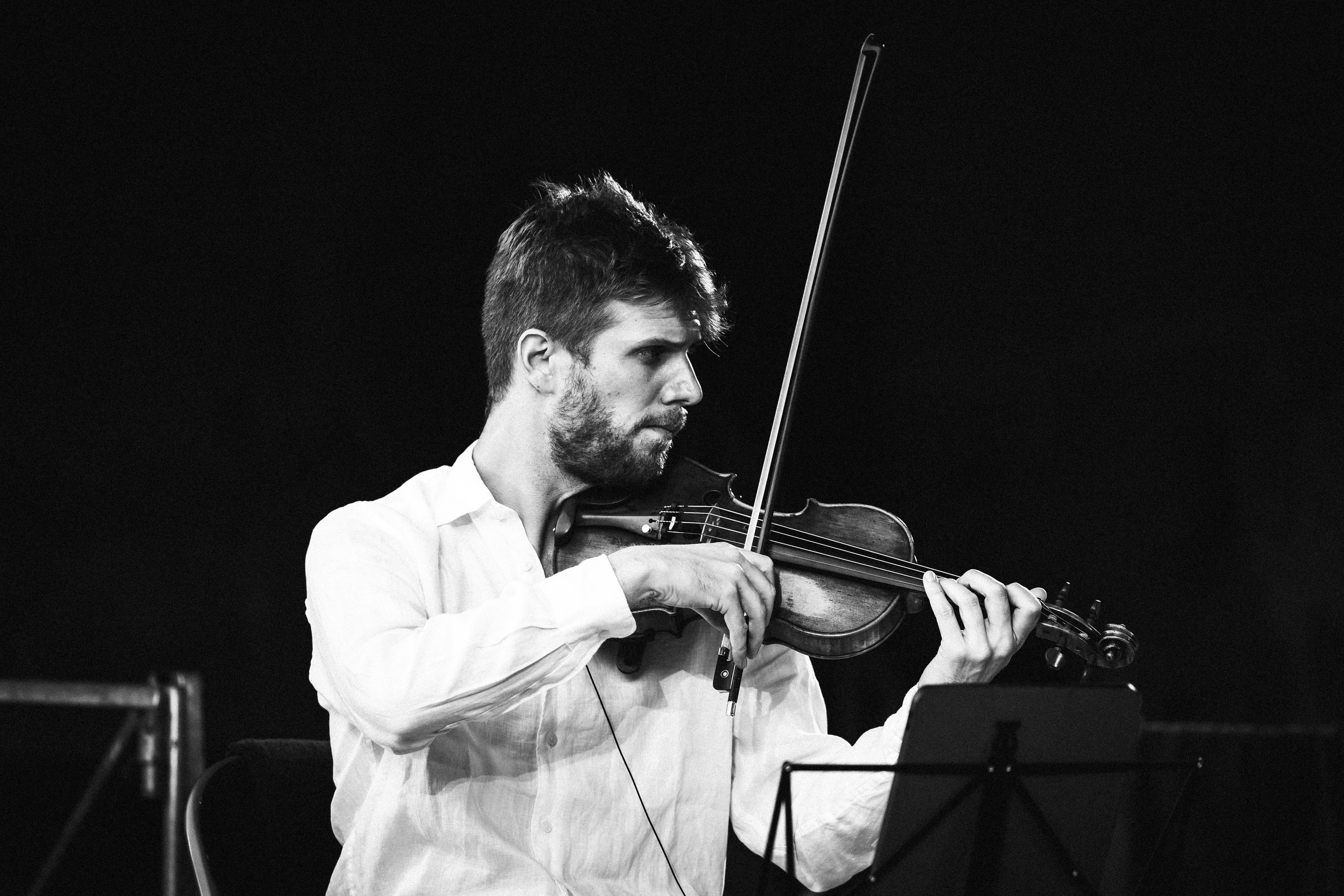 Un homme joué du violon dans un environnement sombre, en noir et blanc.