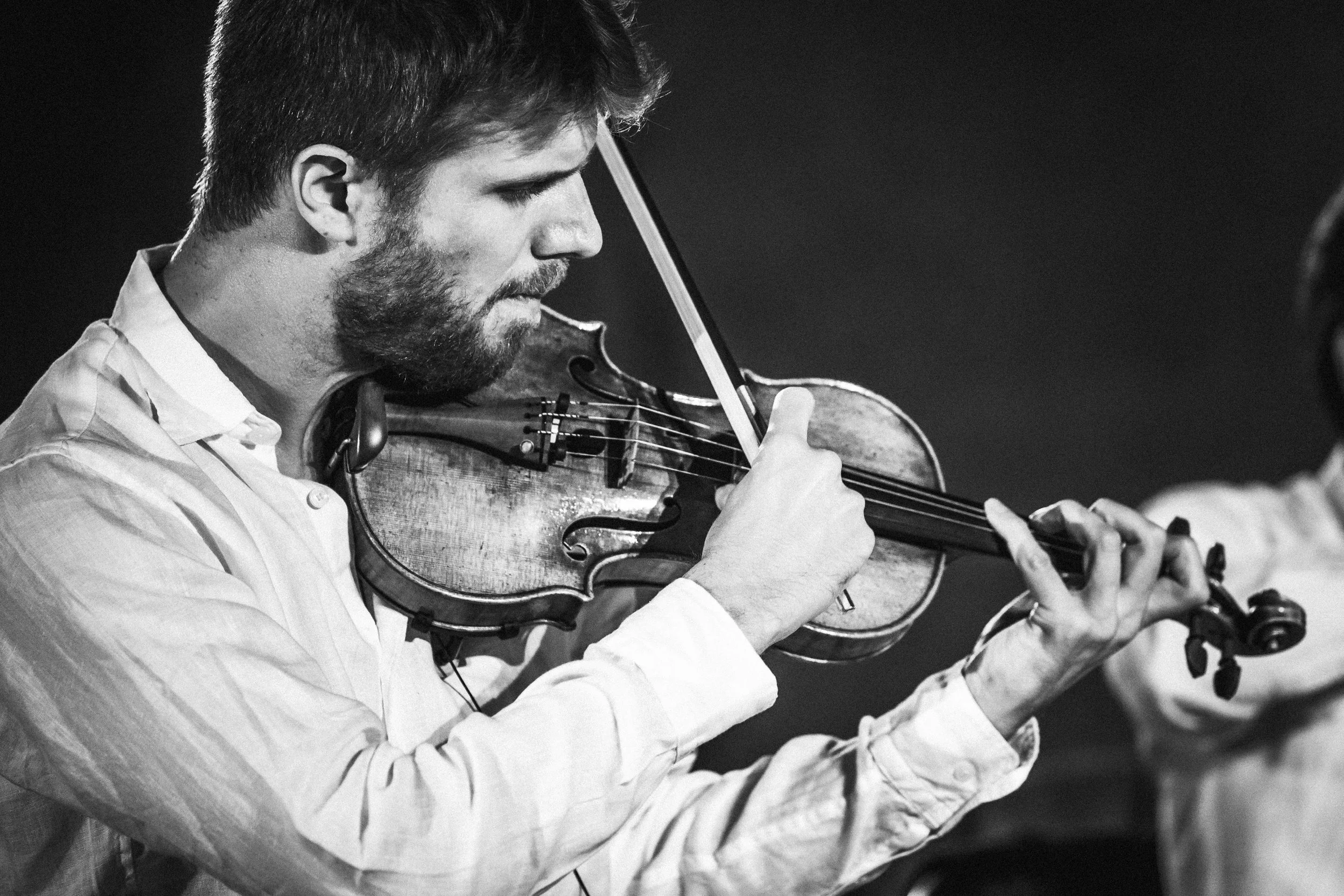 Un homme joue du violon en noir et blanc, se concentrant sur son instrument.