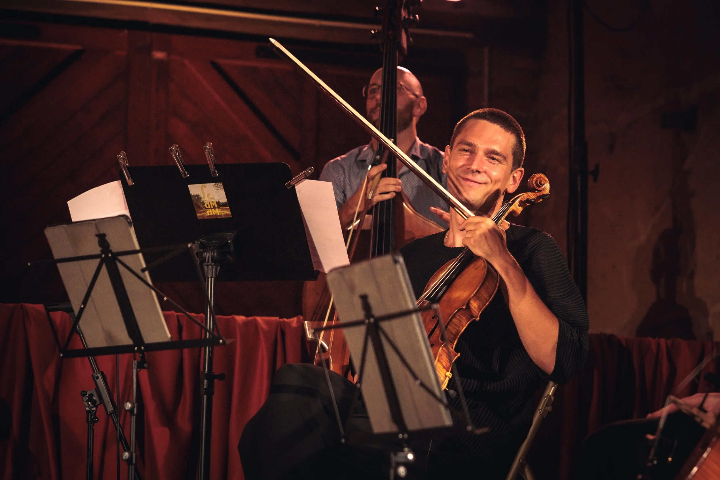 Deux musiciens jouent du violon et de la contrebasse lors d'une performance musicale dans une salle avec un plafond en bois.
