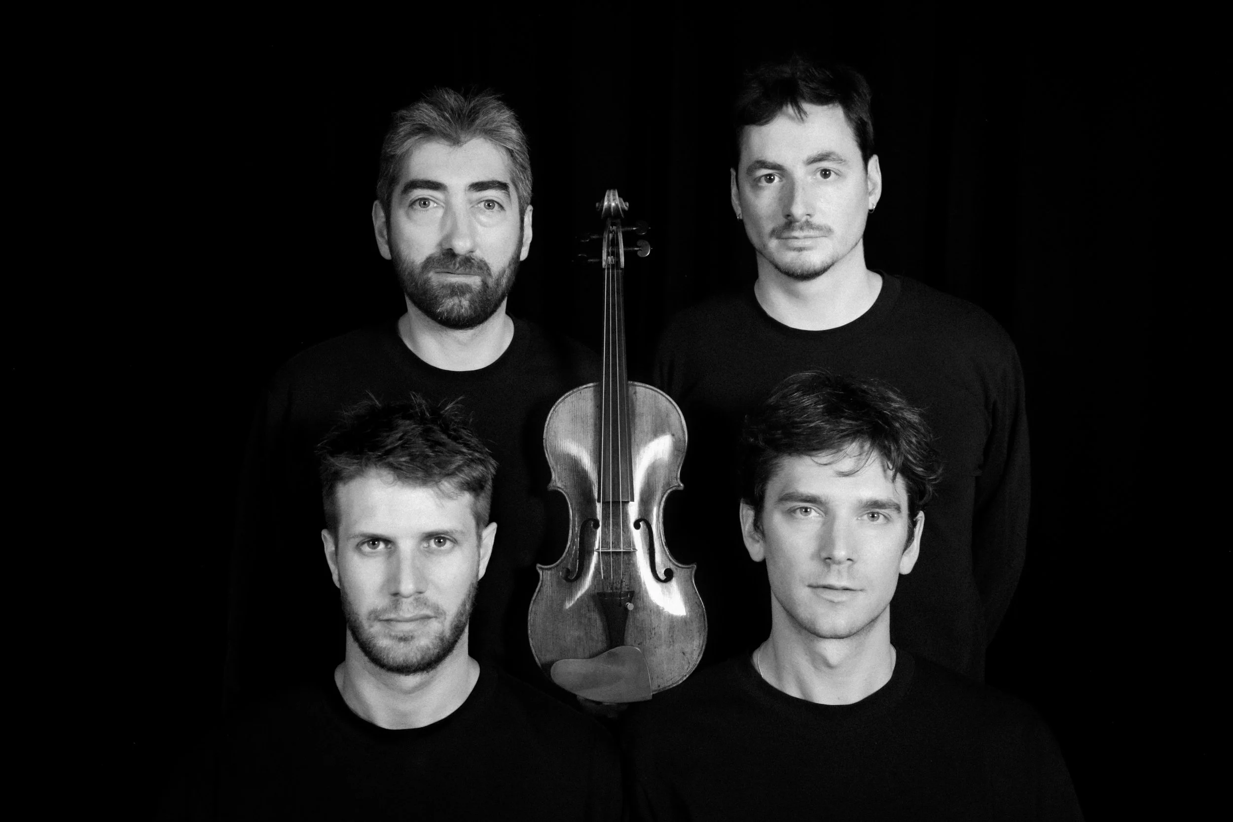 Groupe de cinq hommes avec un violon placé verticalement entre eux, tous portant des vêtements noirs, image en noir et blanc.