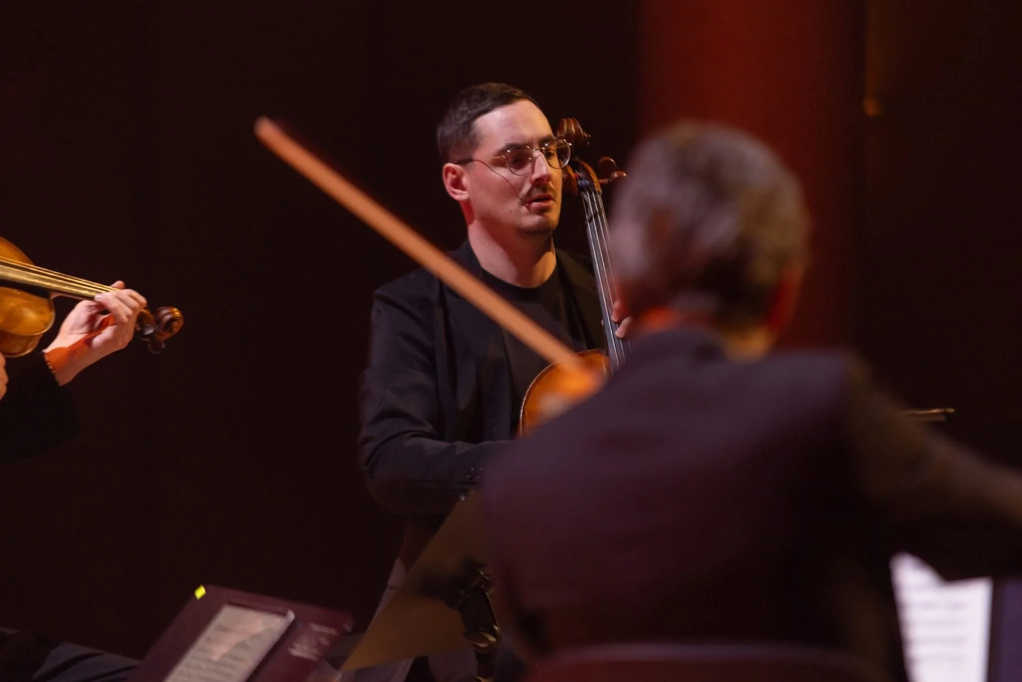 Jeune homme jouant du violon lors d'une performance musicale, portant des lunettes et concentré.