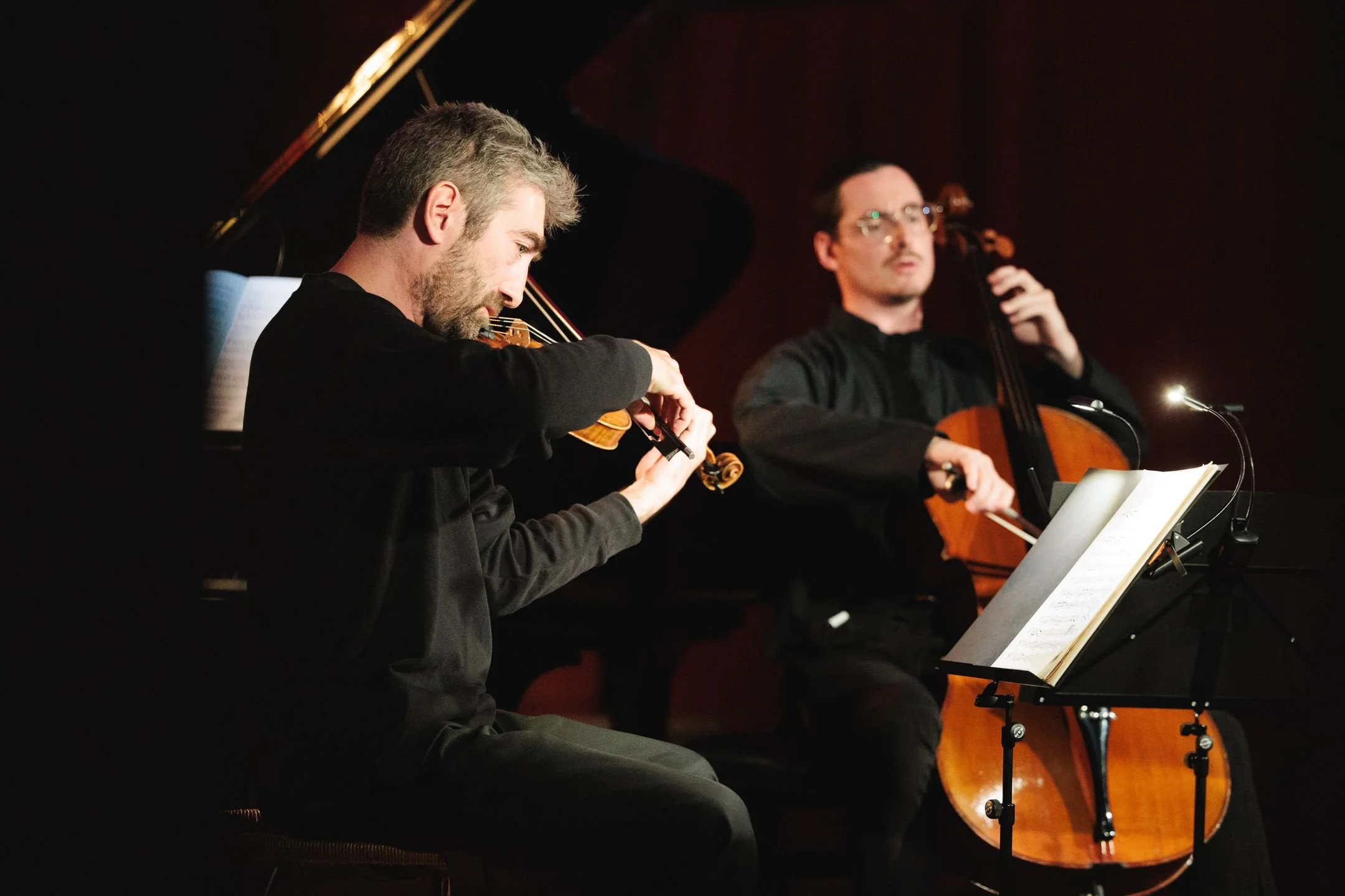 Deux jeunes hommes jouent du violon et du violoncelle lors d'une performance musicale. L'un d'eux lit la musique sur un support.