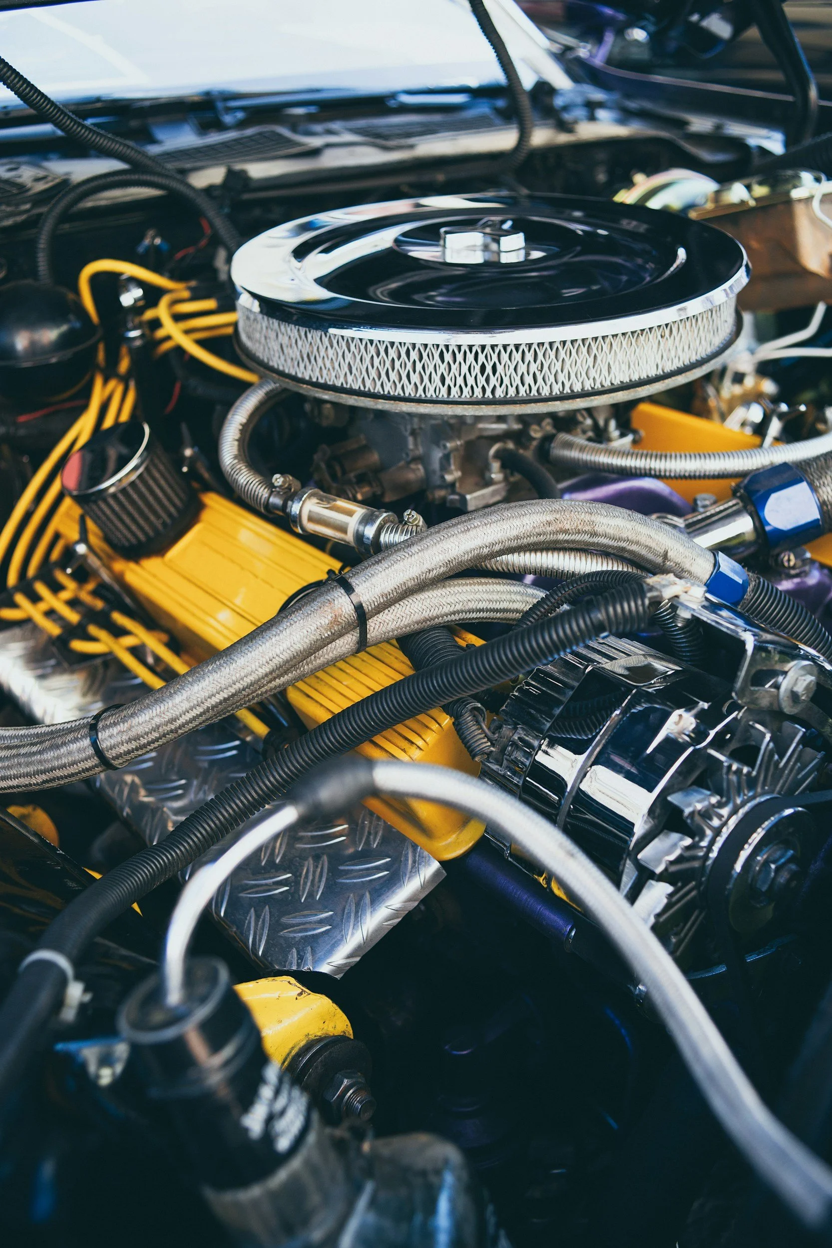 Close-up of a car engine with various hoses, wires, and components, featuring a chrome air filter on top.