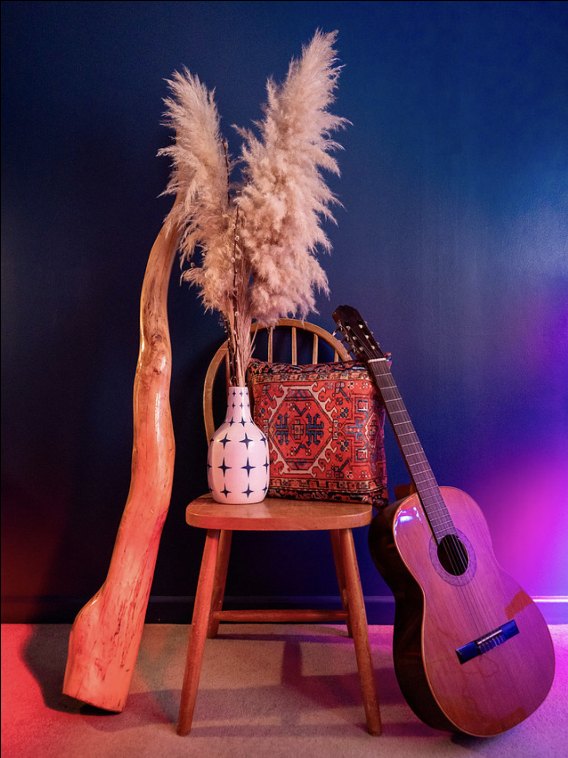 Acoustic guitar and didgeridoo  beside a wooden chair under blue and magenta lighting.
