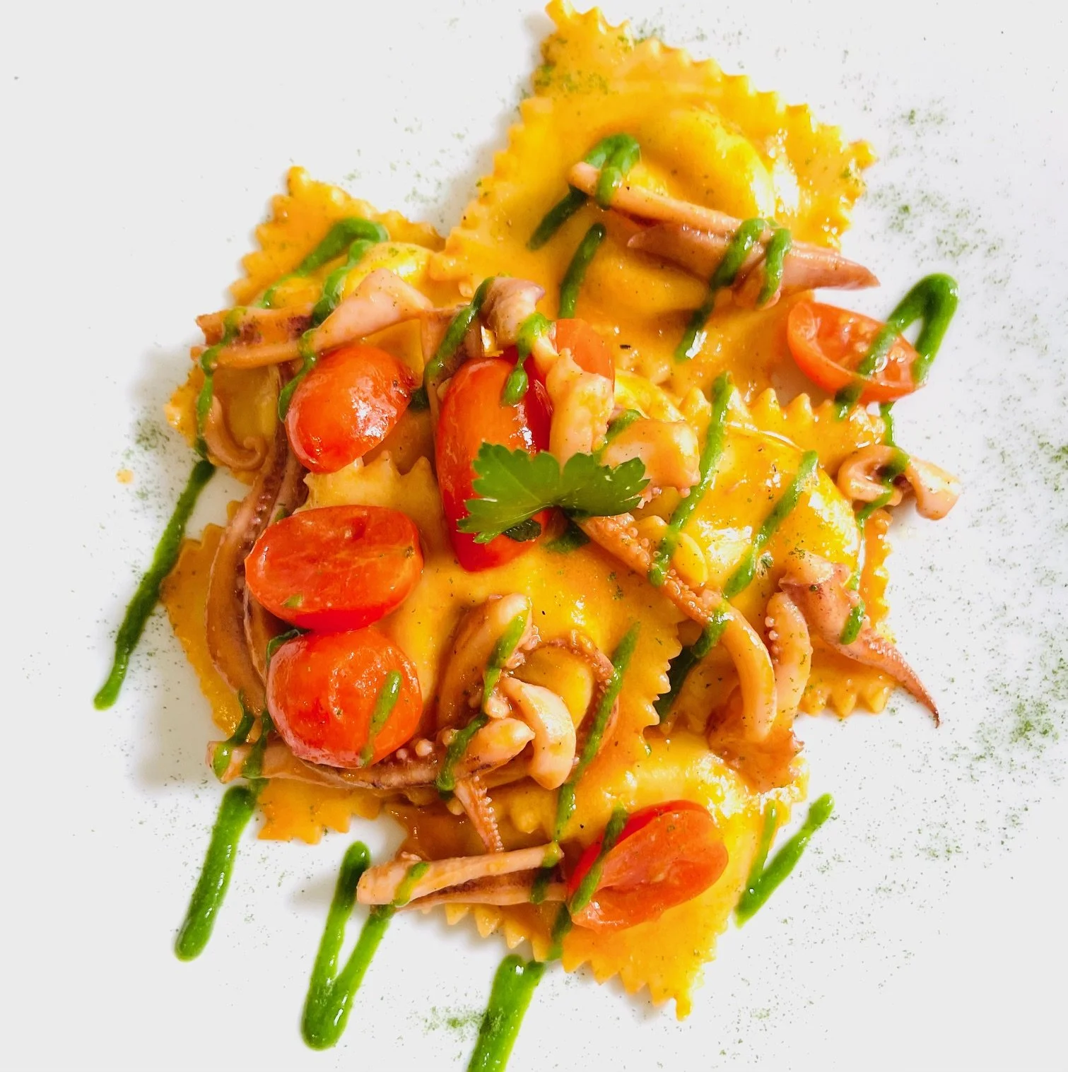 Piatti di pasta con ingredienti come cherry tomato, calamari e foglie di prezzemolo, decorato con salsa verde e servito su piatto bianco.