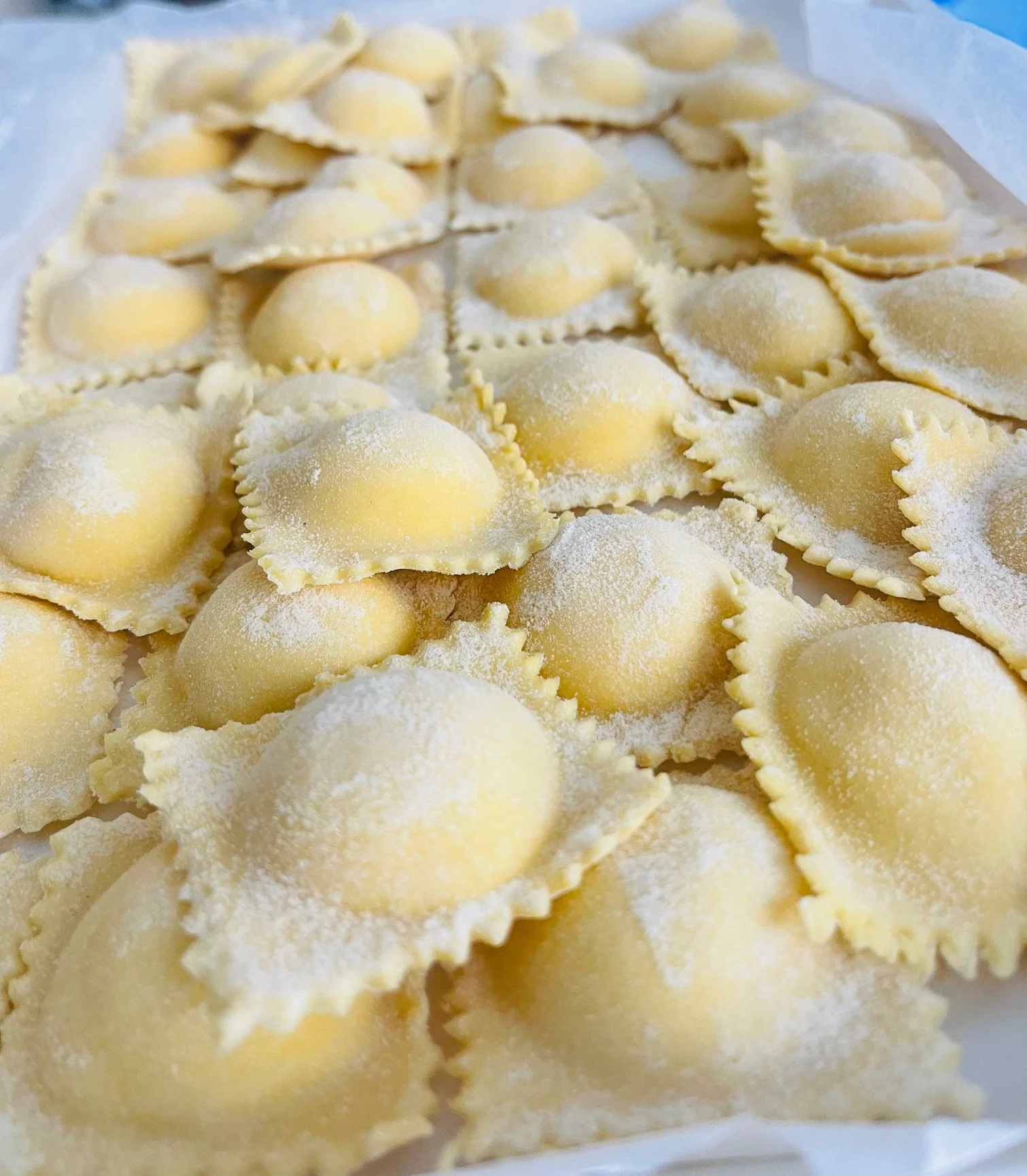 Ravioli freschi con ripieno di formaggio, spolverati con farina, disposti su un vassoio o superficie di lavoro.