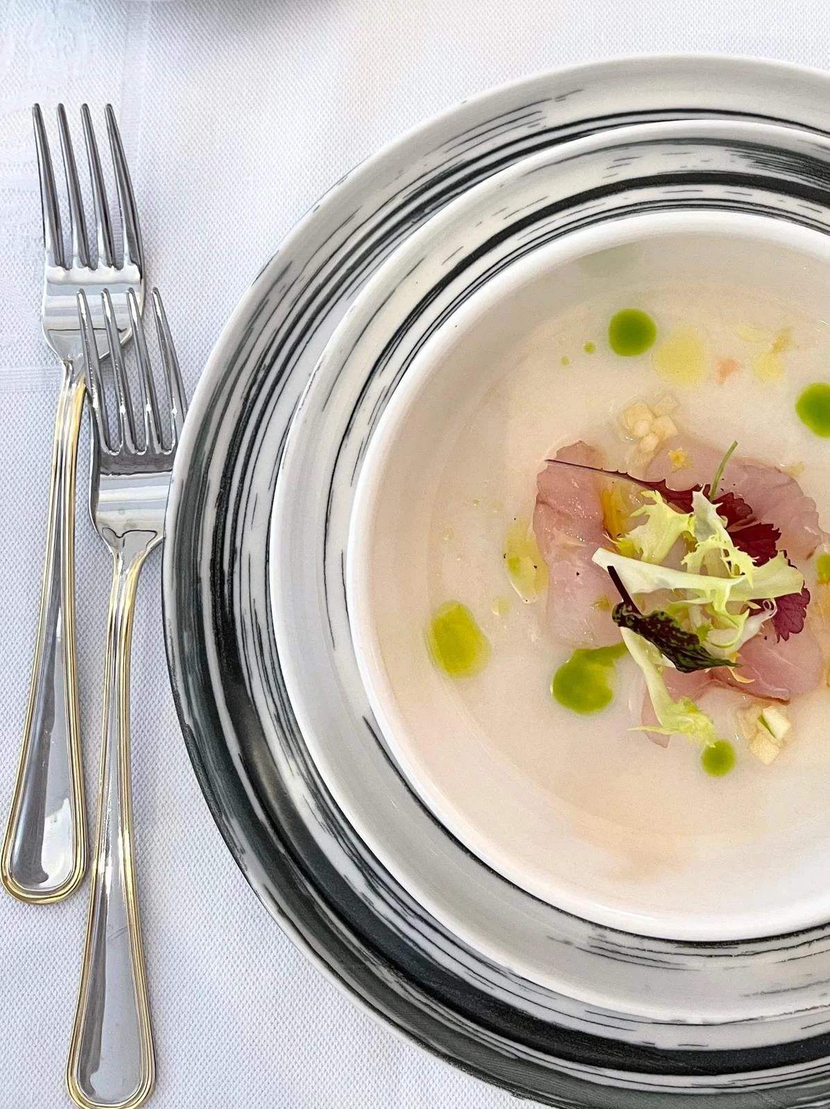 Piatti di cucina elegante con fette di prosciutto, foglie di insalata editi piccole decorazioni verdi, serviti in porcellana con forchette dorate accanto su tovagliolo bianco.