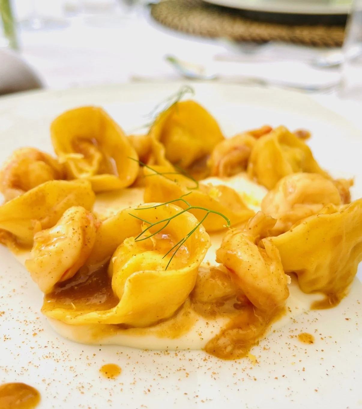 Tortellini di pasta fresca riempiti con ripieno di carne o formaggio, serviti con salsa di burro e salvia, decorati con un rametto di erba aromatica.