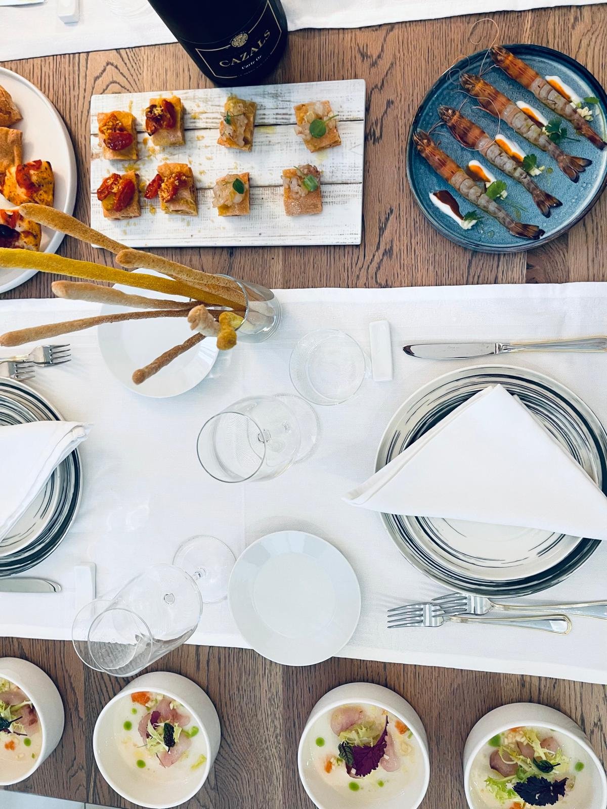 Assortimento di antipasti e finger food su un tavolo apparecchiato elegantemente con bicchieri di vetro e tovaglioli bianchi.