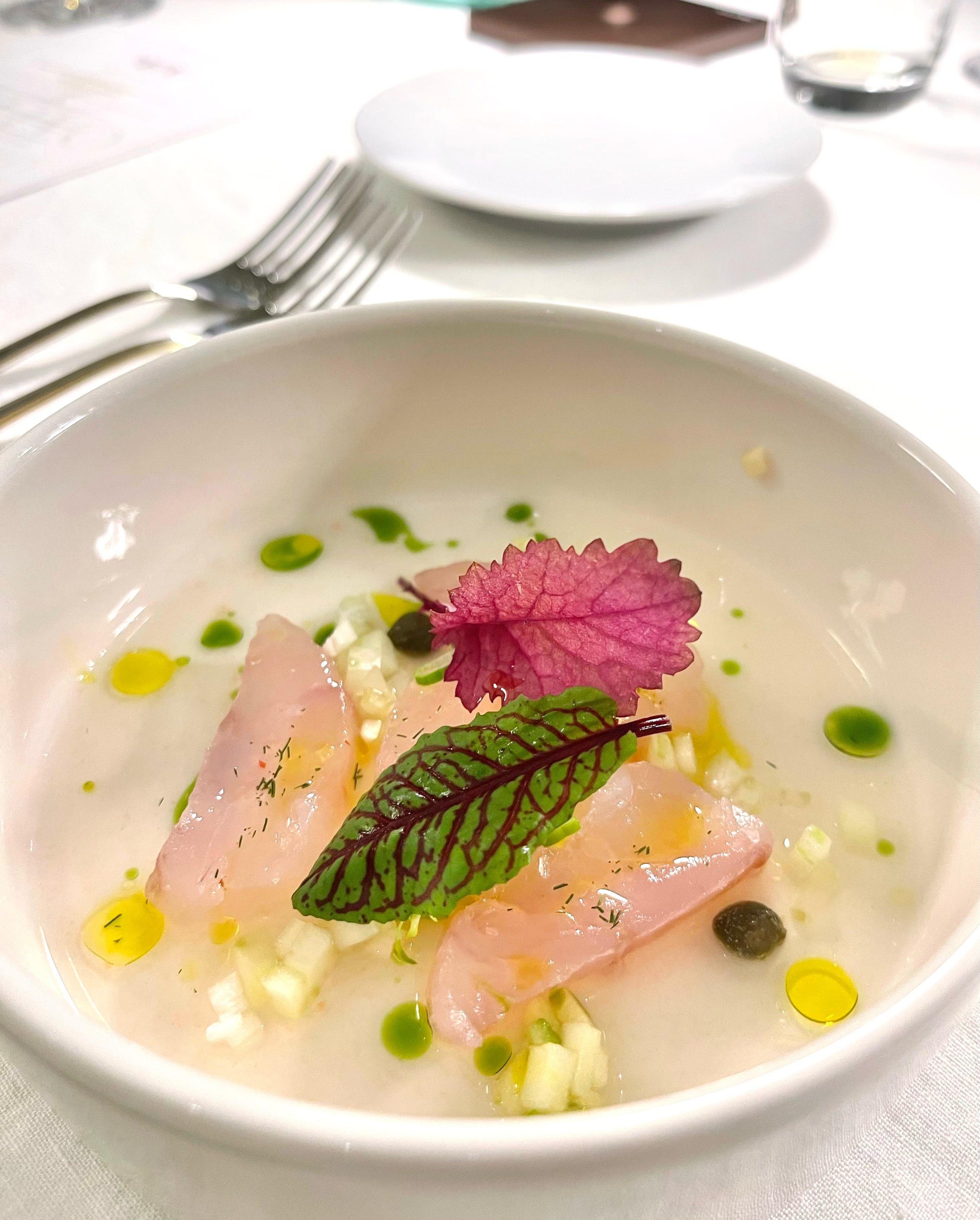 Zuppa cremosa decorata con foglie di erbe, fiori eduli e gocce di olio