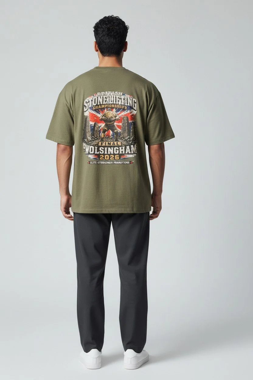 Back view of a man in a green graphic T-shirt, gray pants, and white sneakers, standing against a plain background.