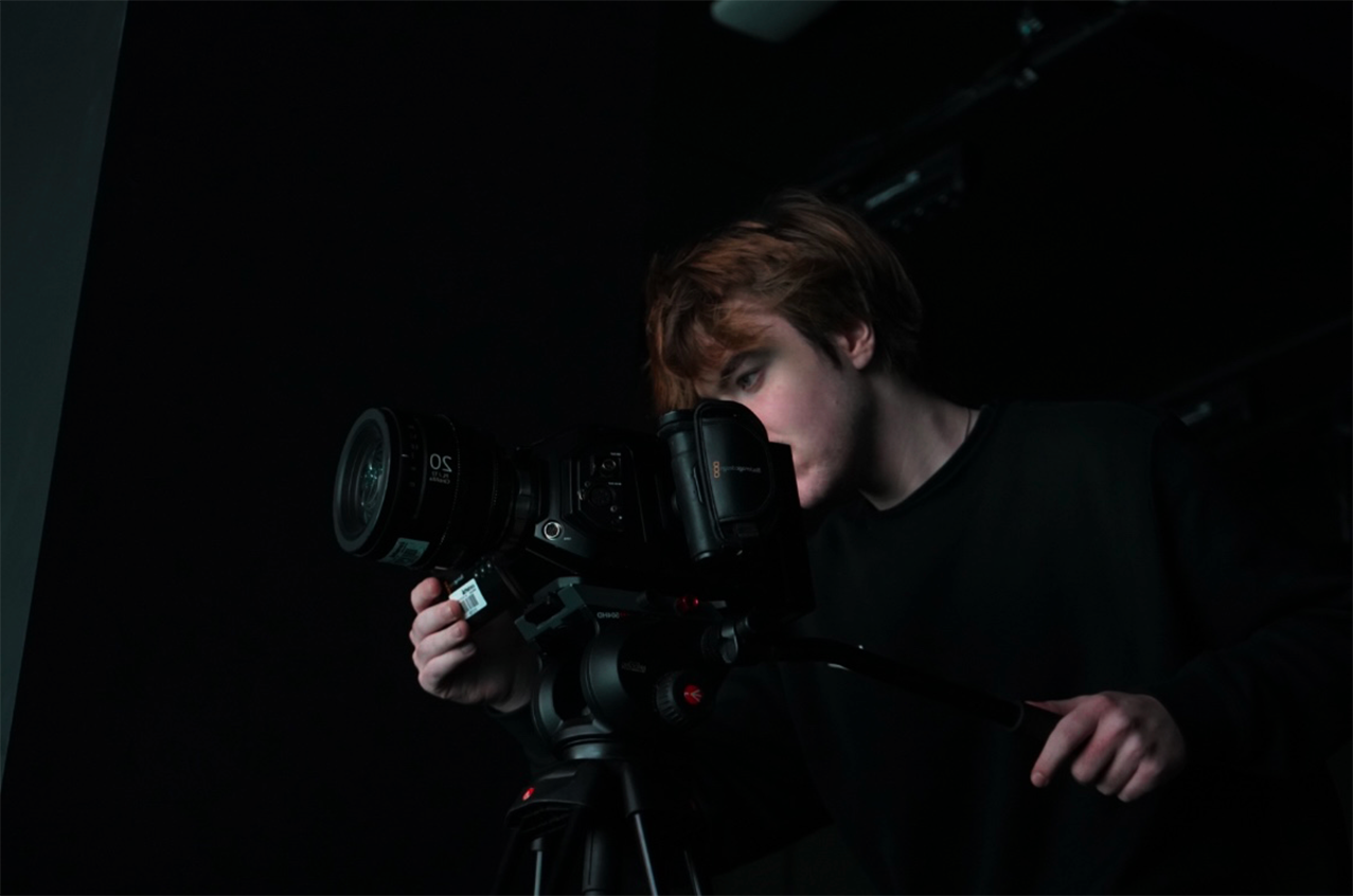 Young man looking through camera on tripod in dark room